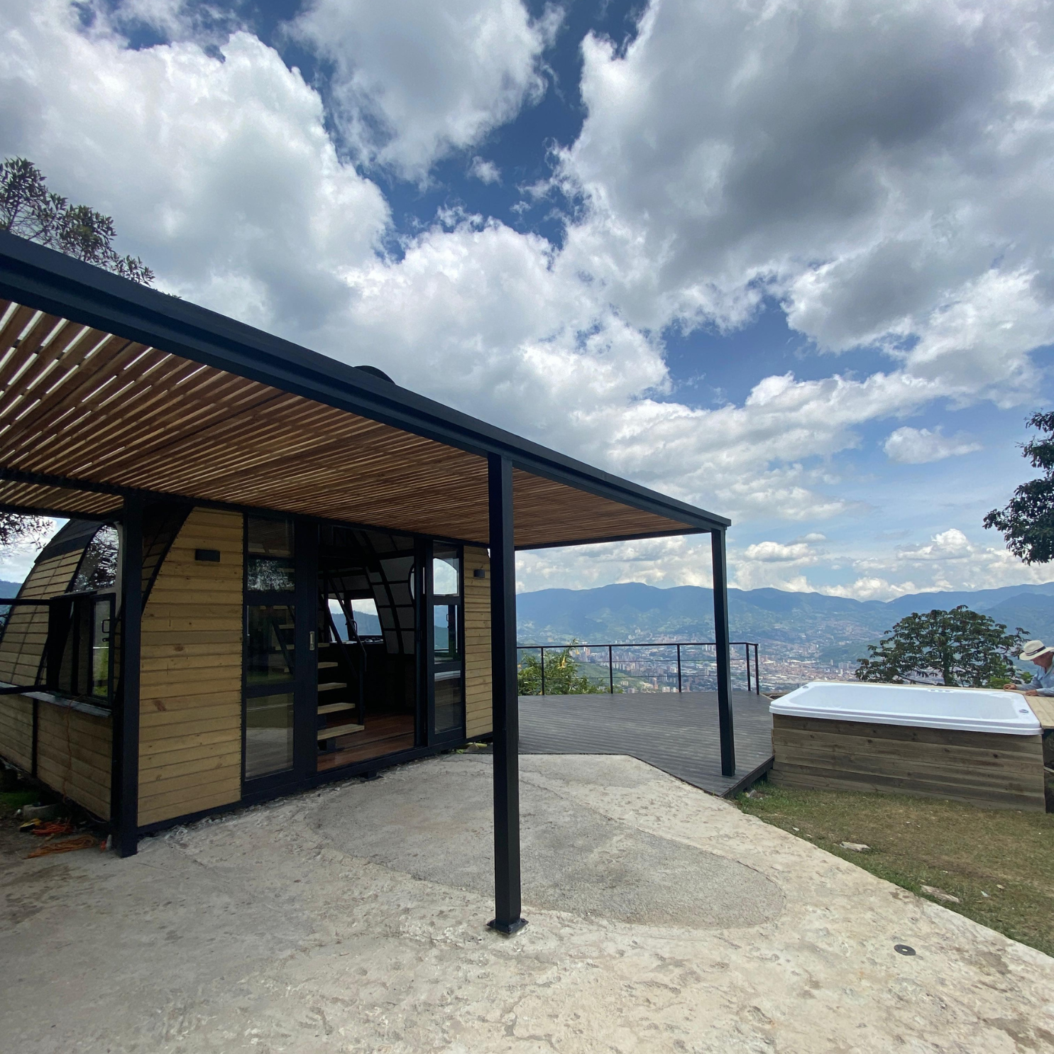 Casa de madera con techo de pérgola, patio con jacuzzi y vista de montaña con cielo nublado.