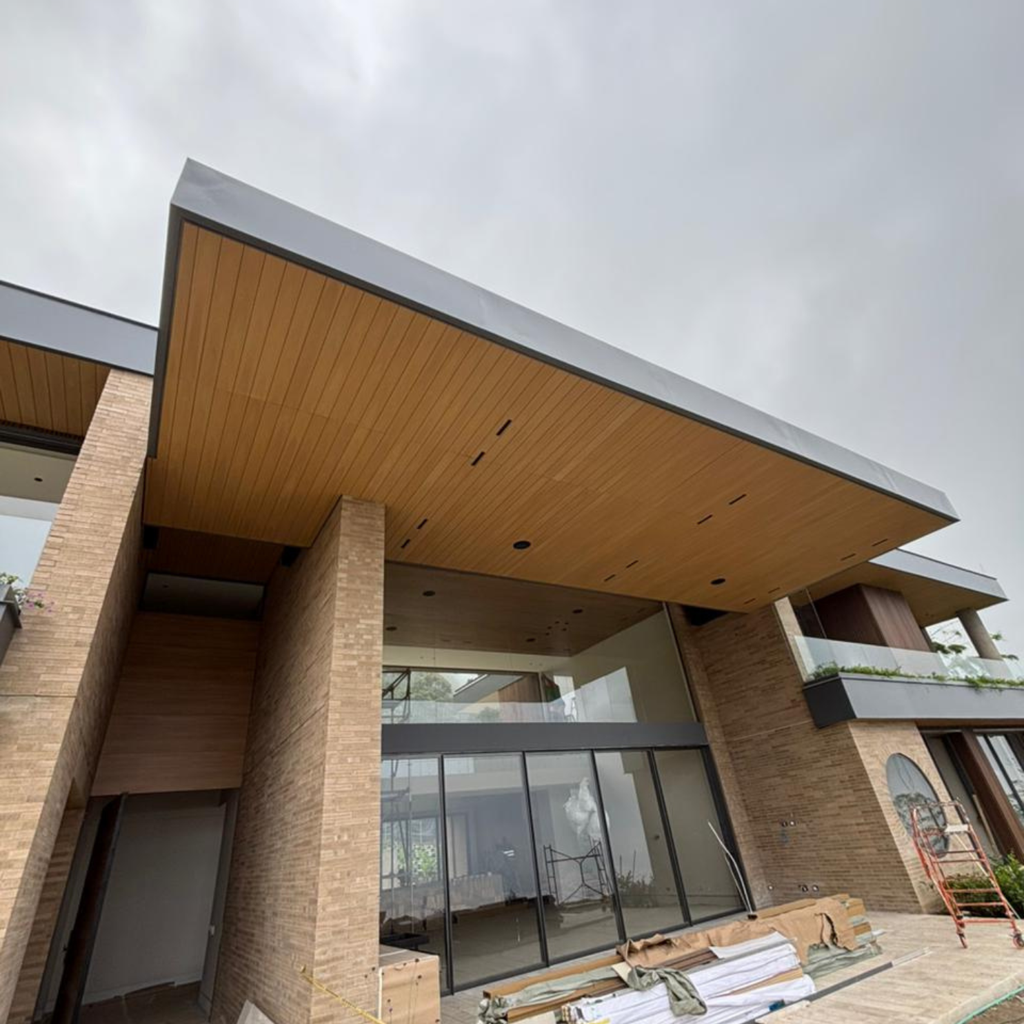 Casa moderna con fachada de ladrillo, techo de madera y grandes ventanales de vidrio.