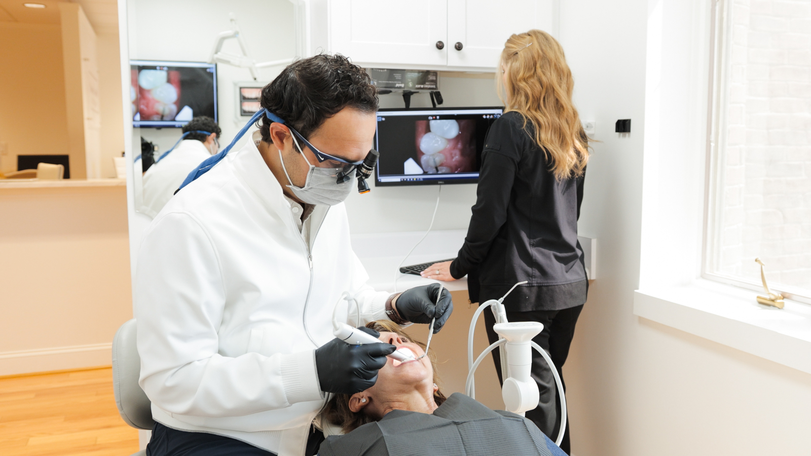 Dentist in white coat discussing treatment with smiling patient at Brentwood Aesthetic & Family Dentists