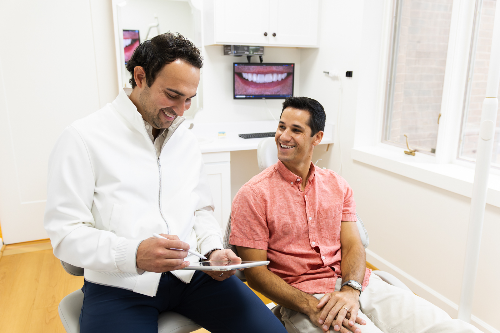 Dentist in white coat discussing treatment with smiling patient at Brentwood Aesthetic & Family Dentists