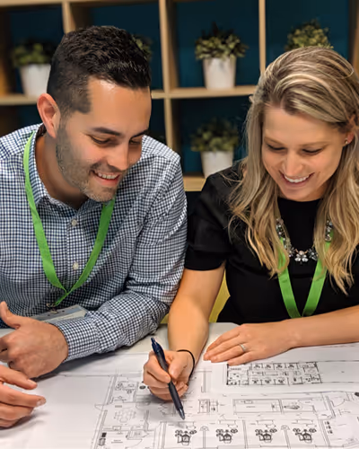 A man and a woman sitting at a table working on a blueprint.