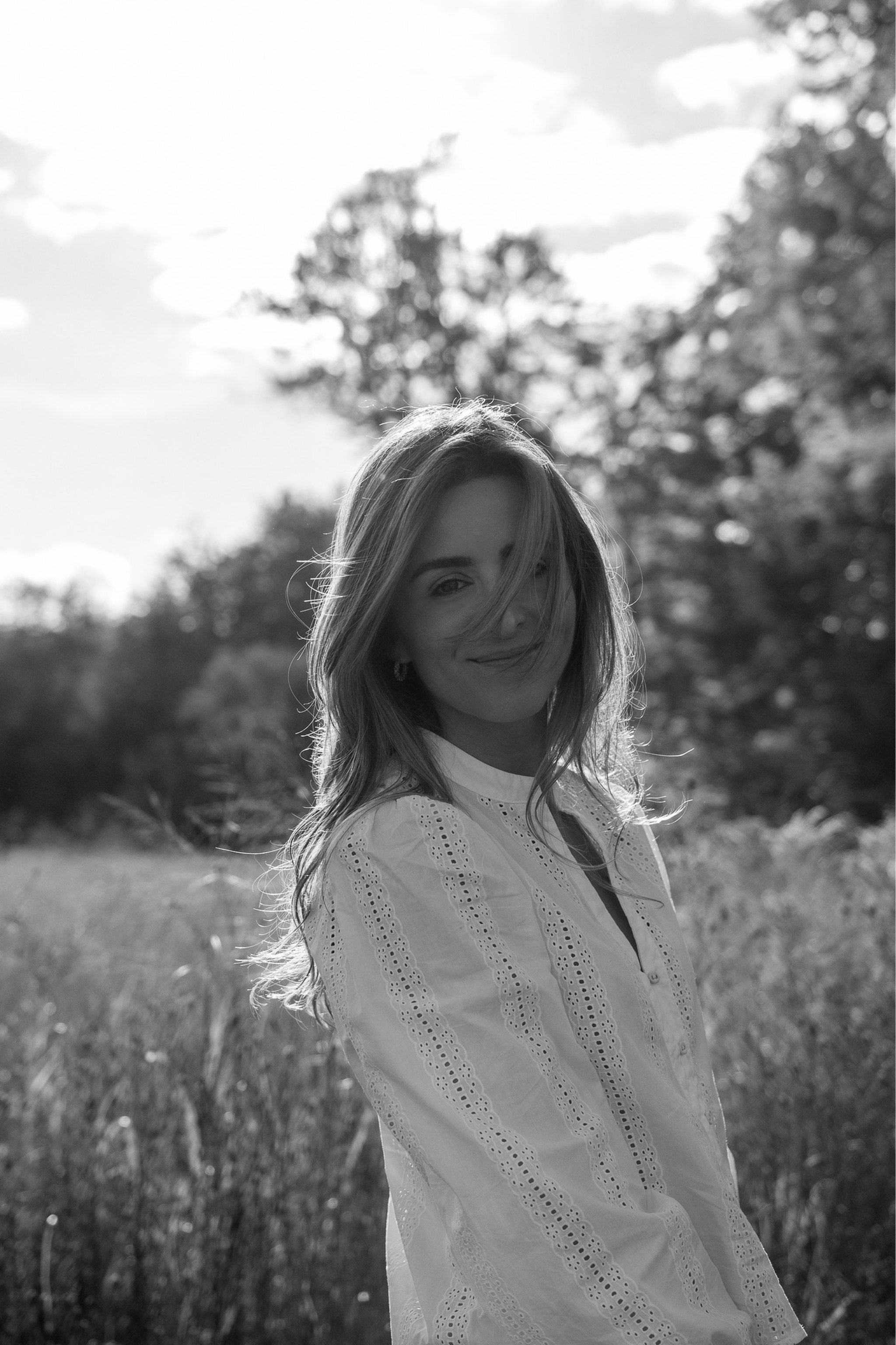 Barbara Rodriguez with long hair smiling in a sunlit field, wearing a white eyelet patterned blouse.
