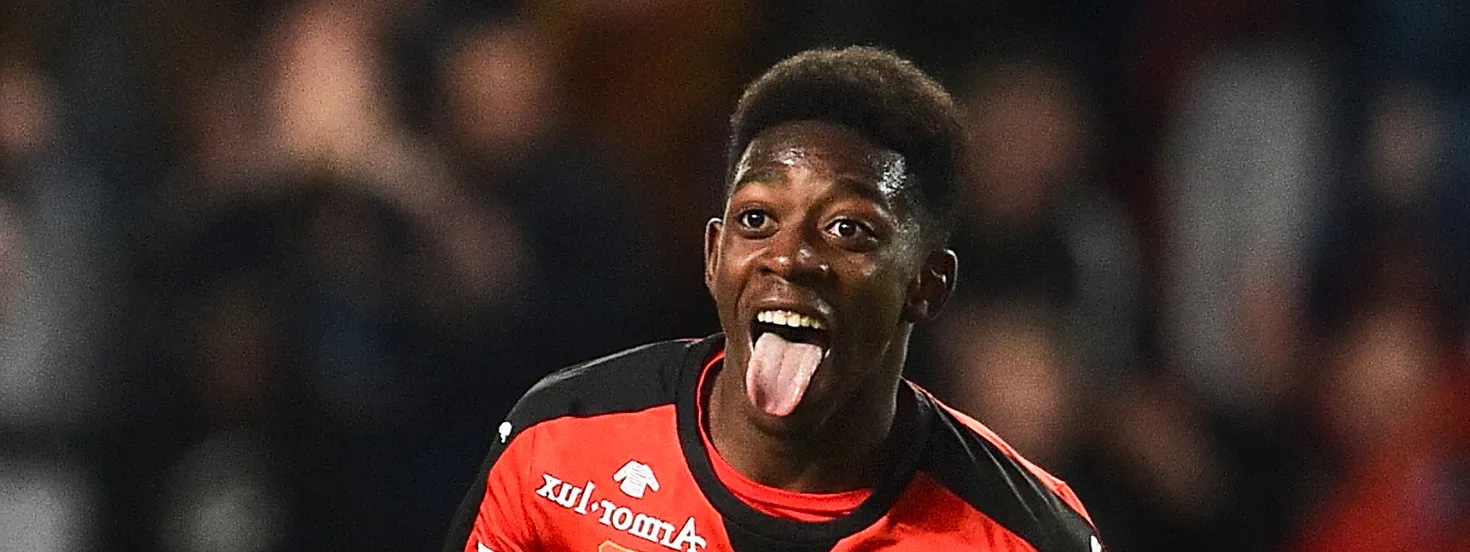 Soccer player in red and black jersey celebrating with tongue out during a match.