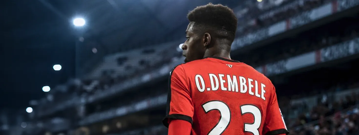 Soccer player O. Dembele wearing red jersey number 23 looking to the side in a stadium at night.