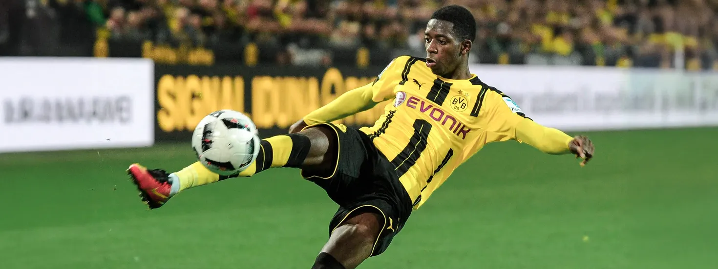 Soccer player in yellow and black Borussia Dortmund uniform kicking a ball mid-air on the field.
