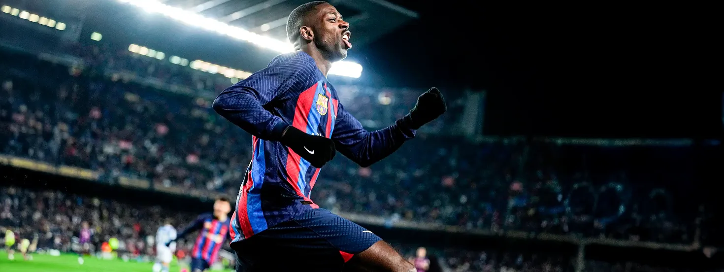 Soccer player in blue and red striped uniform celebrating with a clenched fist in a stadium at night.
