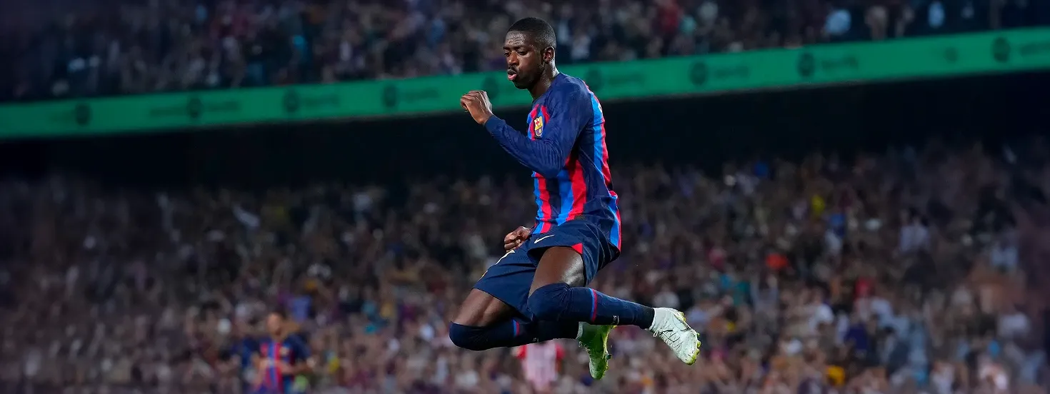 Soccer player in blue and red striped uniform jumping mid-air during a match with a blurred crowd in the background.