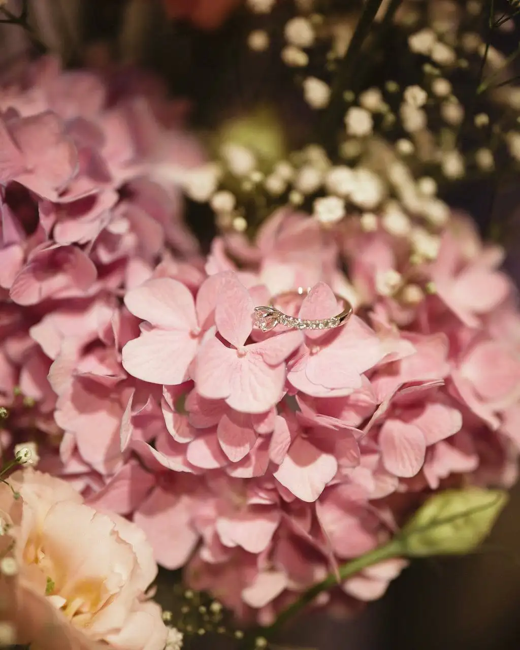 Diamond engagement ring with pavé band resting on a blush pink hydrangea bloom surrounded by baby's breath and roses at a luxury proposal event by Perla Signature Events in Yerevan, Armenia
