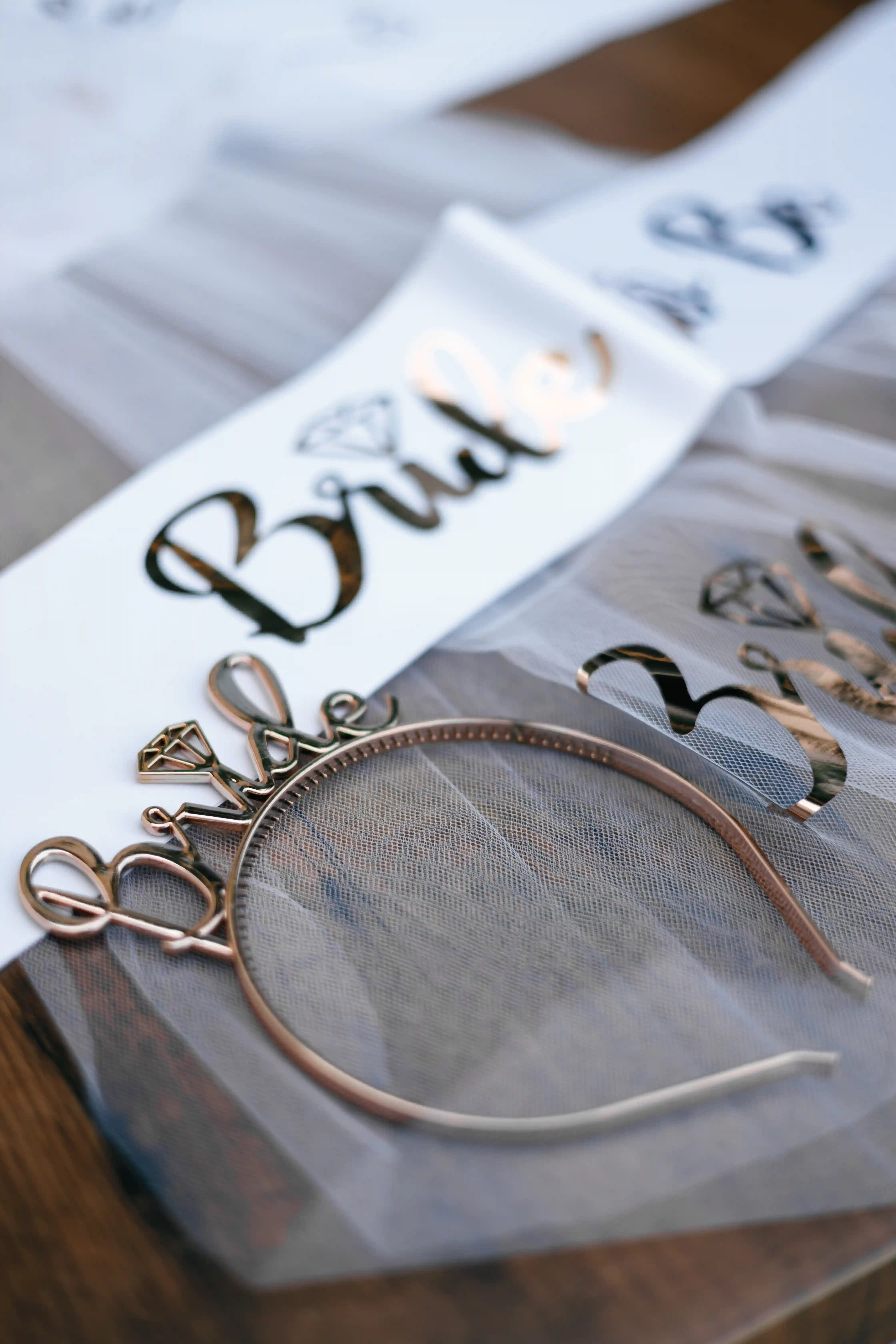 Rose gold wire Bride headband with diamond charm and gold foil Bride sash laid on white tulle as luxury bachelorette party accessories styled by Perla Signature Events in Yerevan, Armenia