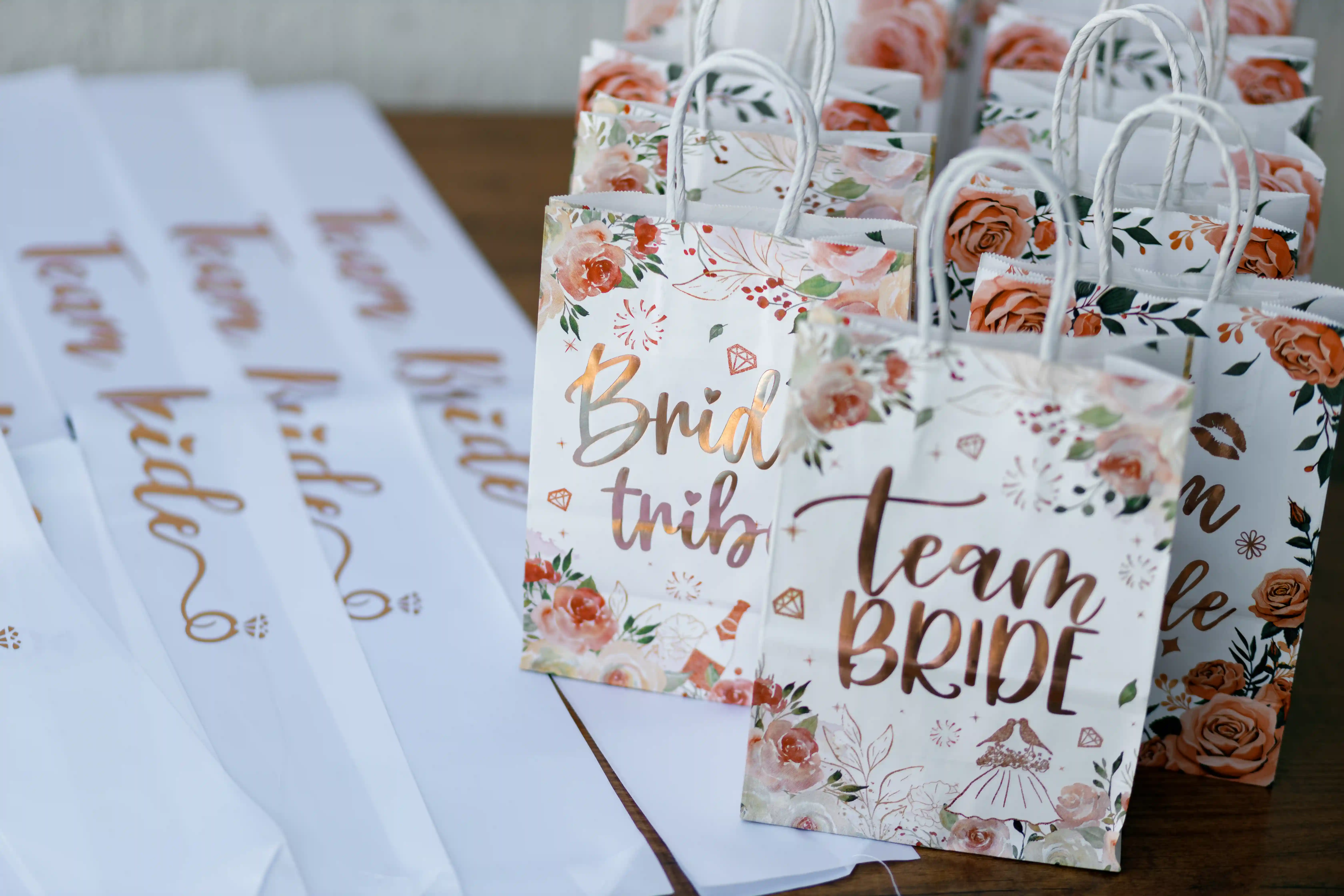 Rose gold `Team Bride` and `Bride Tribe` floral gift bags with matching sashes laid out as bridesmaid favors at a luxury bridal shower planned by Perla Signature Events in Armenia