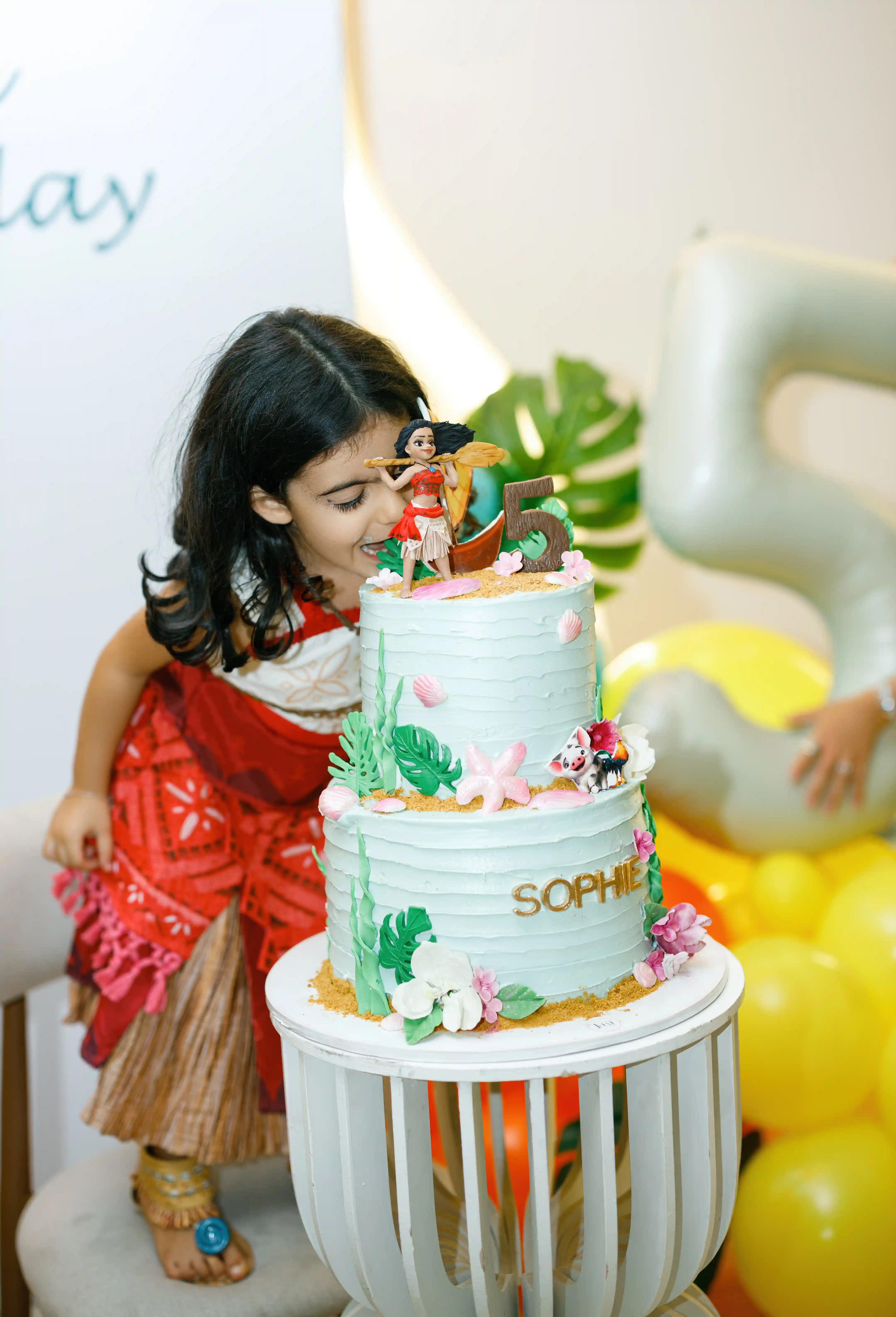 Little girl in a themed costume admiring a two-tier tropical birthday cake with floral decorations at a luxury children's party planned by Perla Signature Events in Armenia