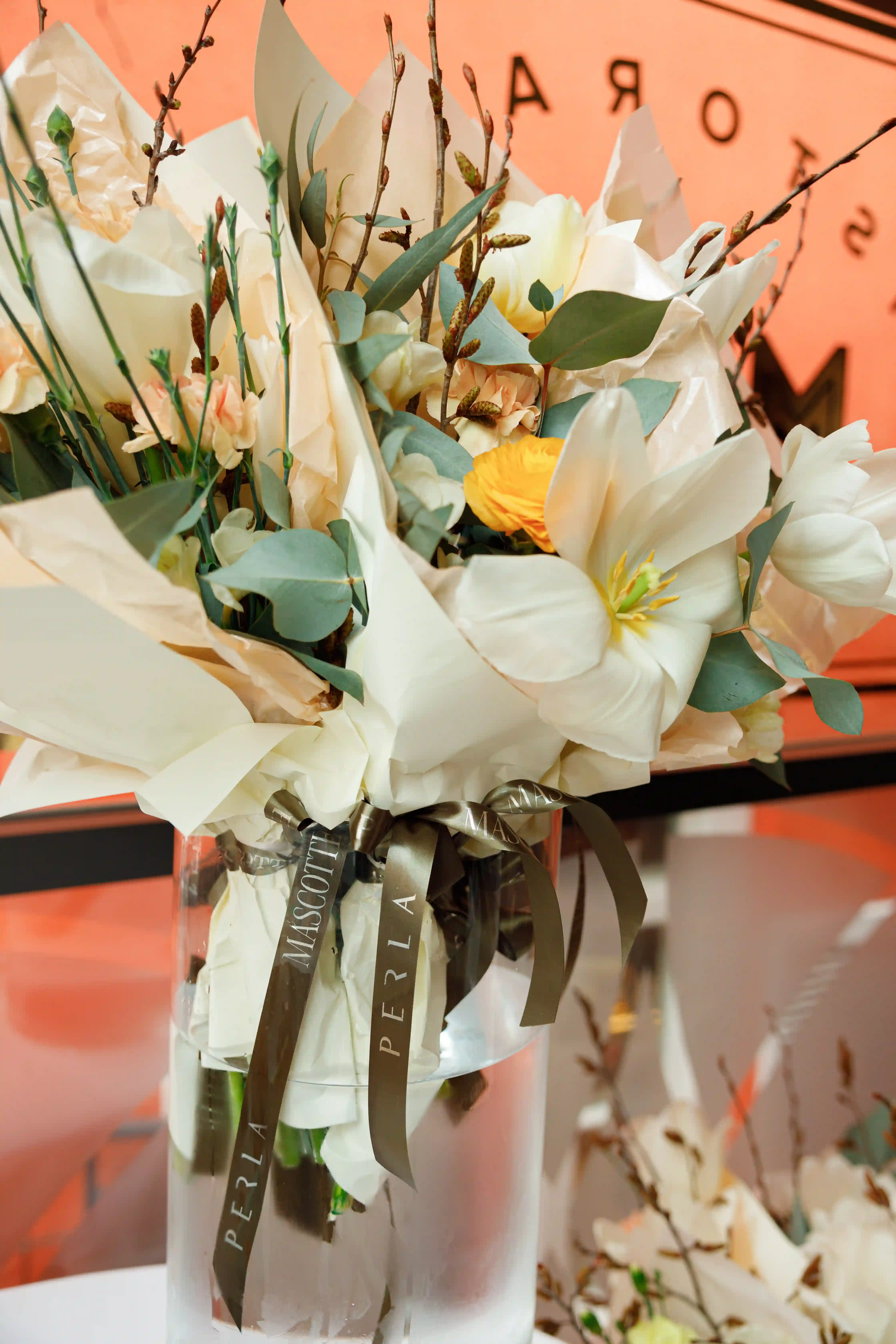 Luxury wrapped bouquet of white tulips, yellow ranunculus, eucalyptus, and willow branches tied with a Perla Signature Events branded olive ribbon at a high-end event in Yerevan, Armenia