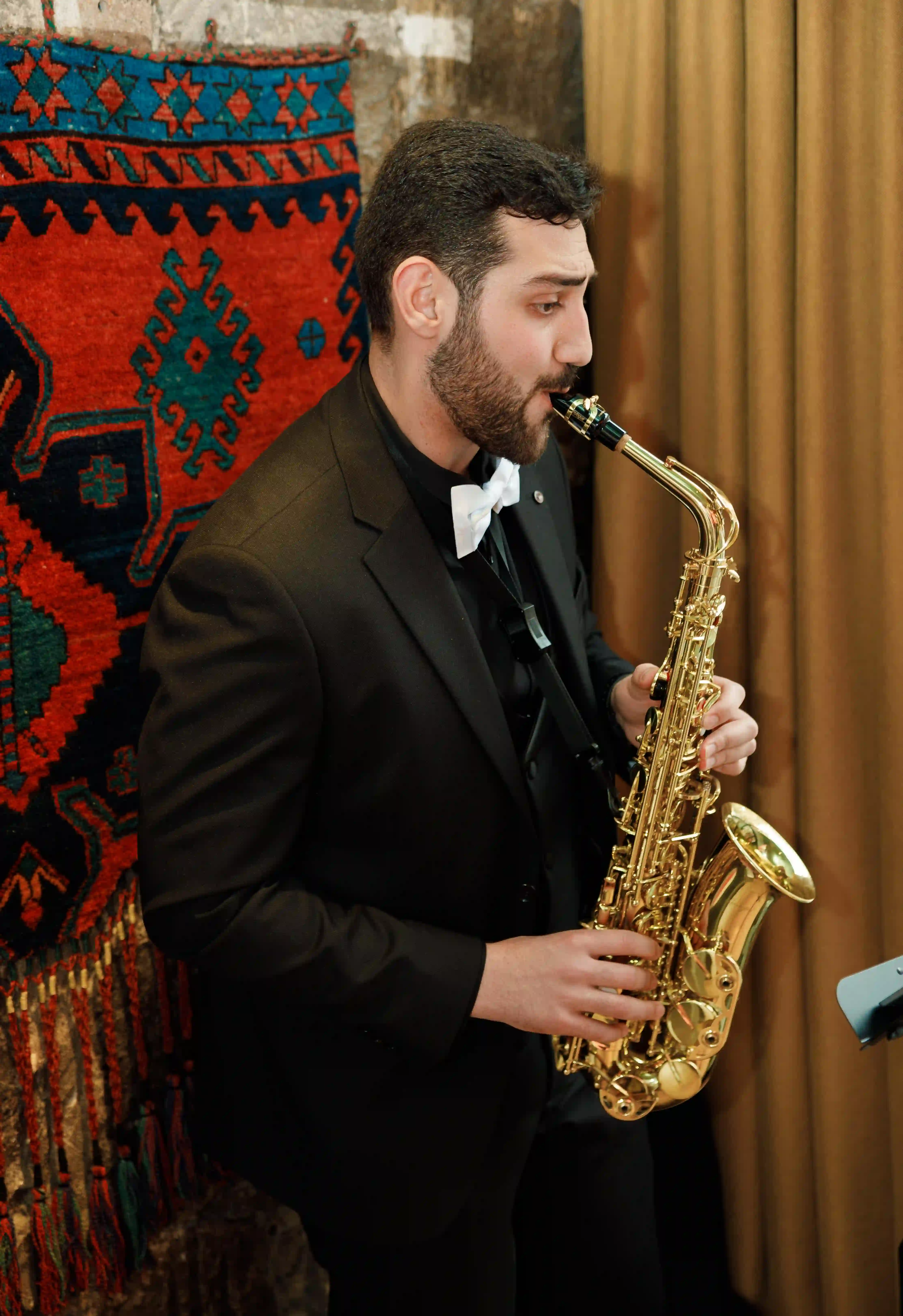 Live saxophonist in a black tuxedo and white bow tie performing against a traditional Armenian carpet backdrop at a luxury event by Perla Signature Events in Yerevan, Armenia