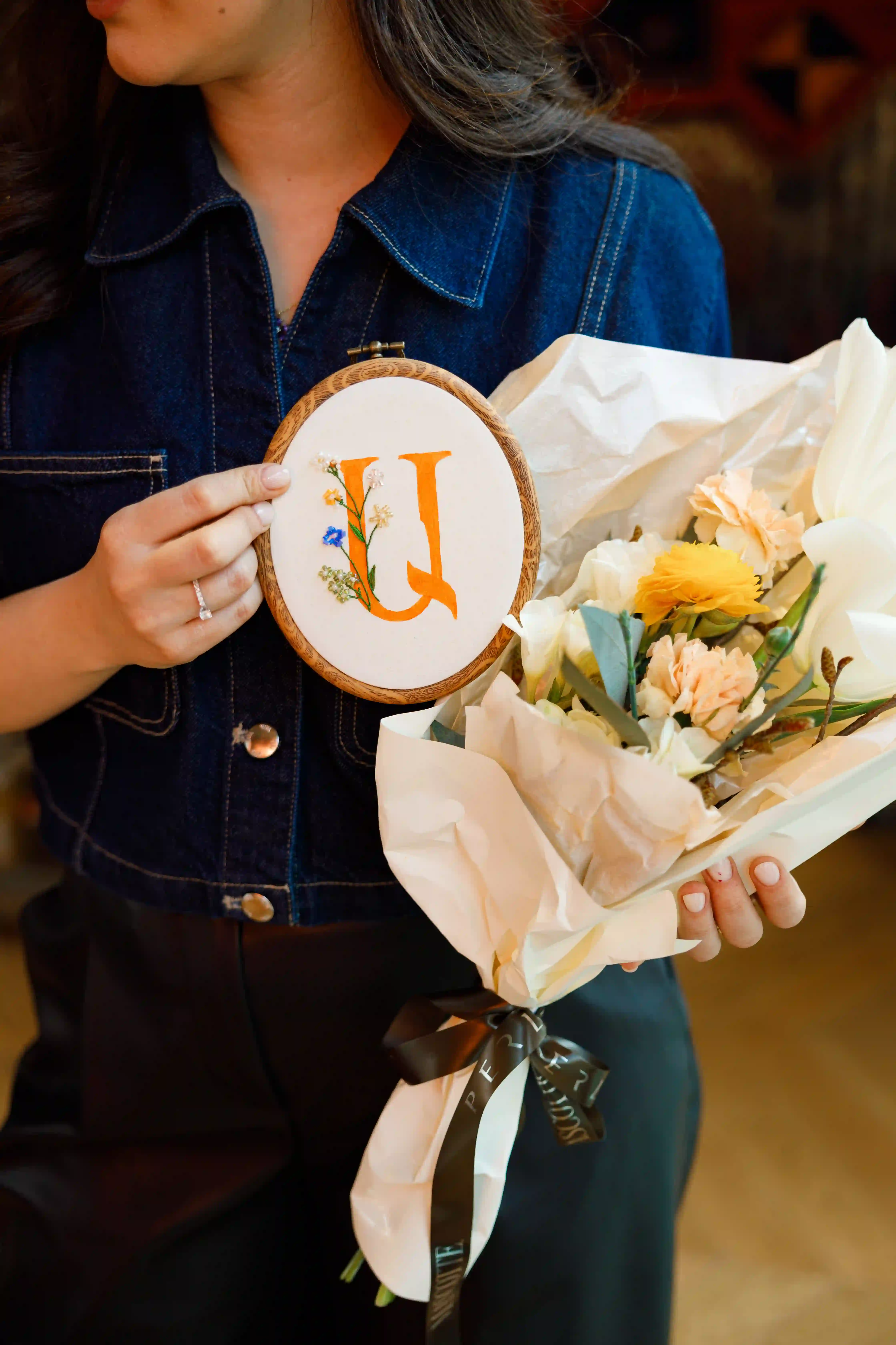 Guest holding a personalized embroidery hoop monogram and a Perla Signature Events ribbon-tied flower bouquet as a bespoke keepsake gift at a luxury event in Yerevan, Armenia
