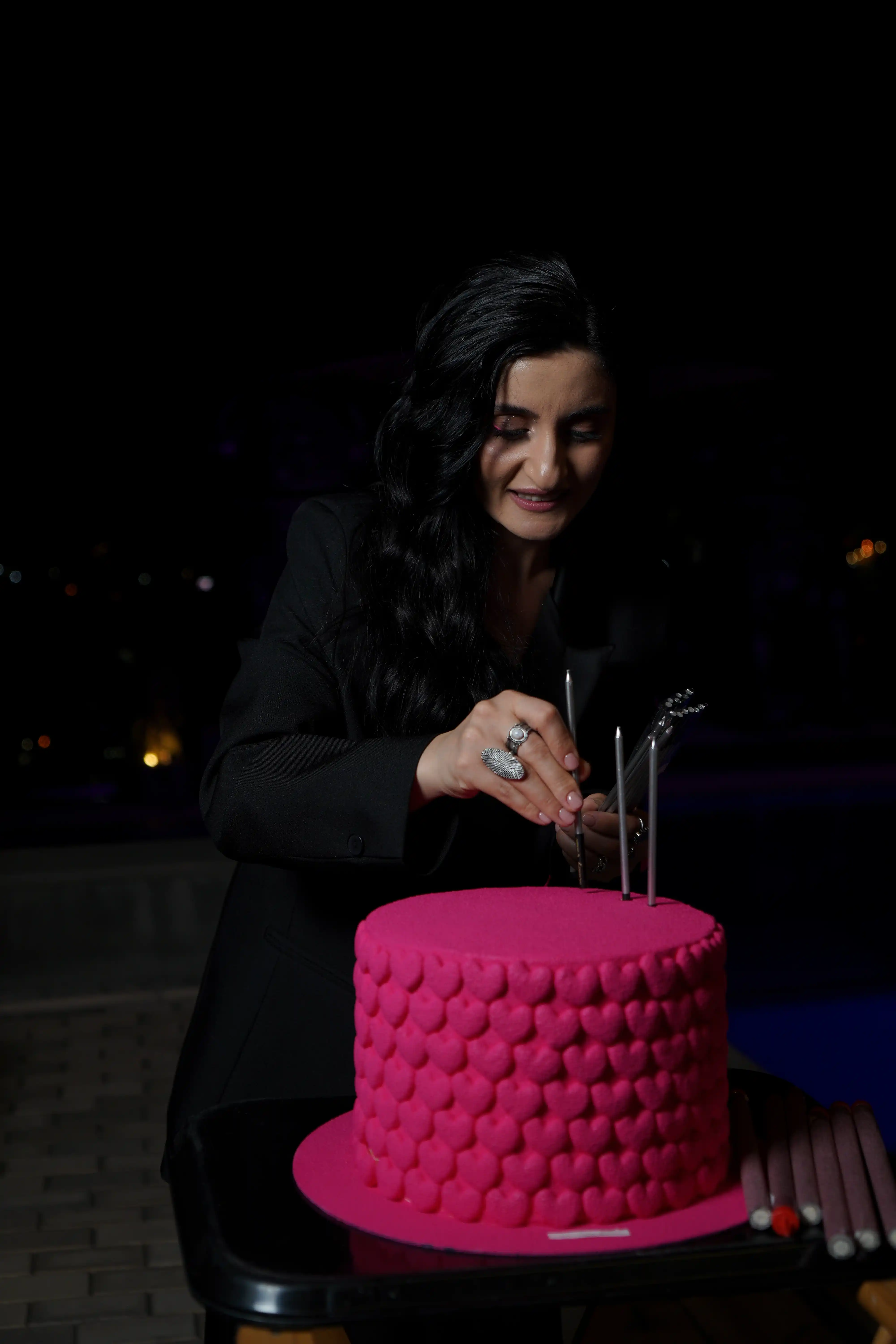 Elegantly dressed woman lighting candles on a bold hot pink textured fondant cake at an outdoor luxury night event by Perla Signature Events in Yerevan, Armenia