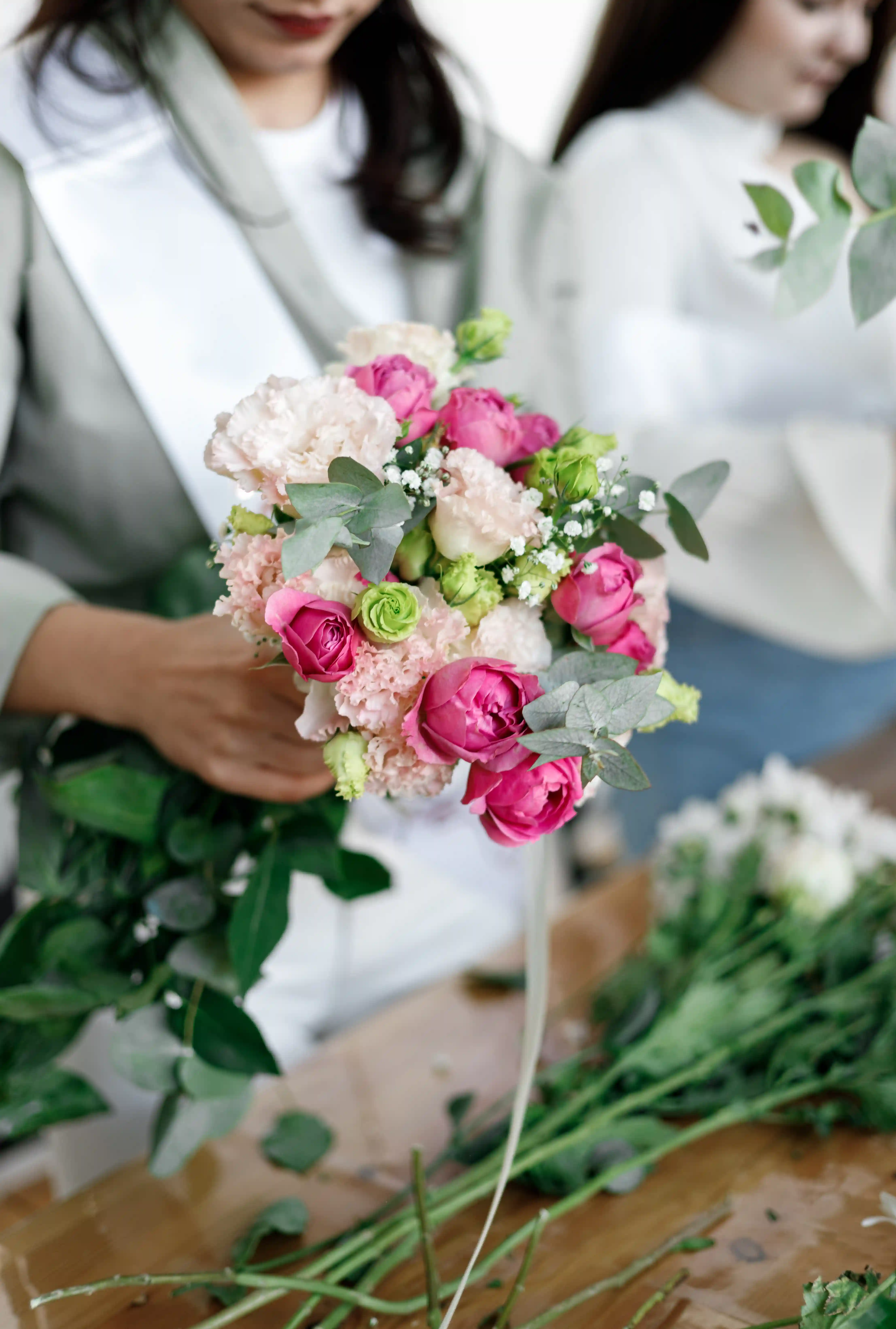 Bride-to-be in a white sash arranging a pink peony and eucalyptus bouquet at a luxury floral workshop bridal shower planned by Perla Signature Events in Yerevan, Armenia