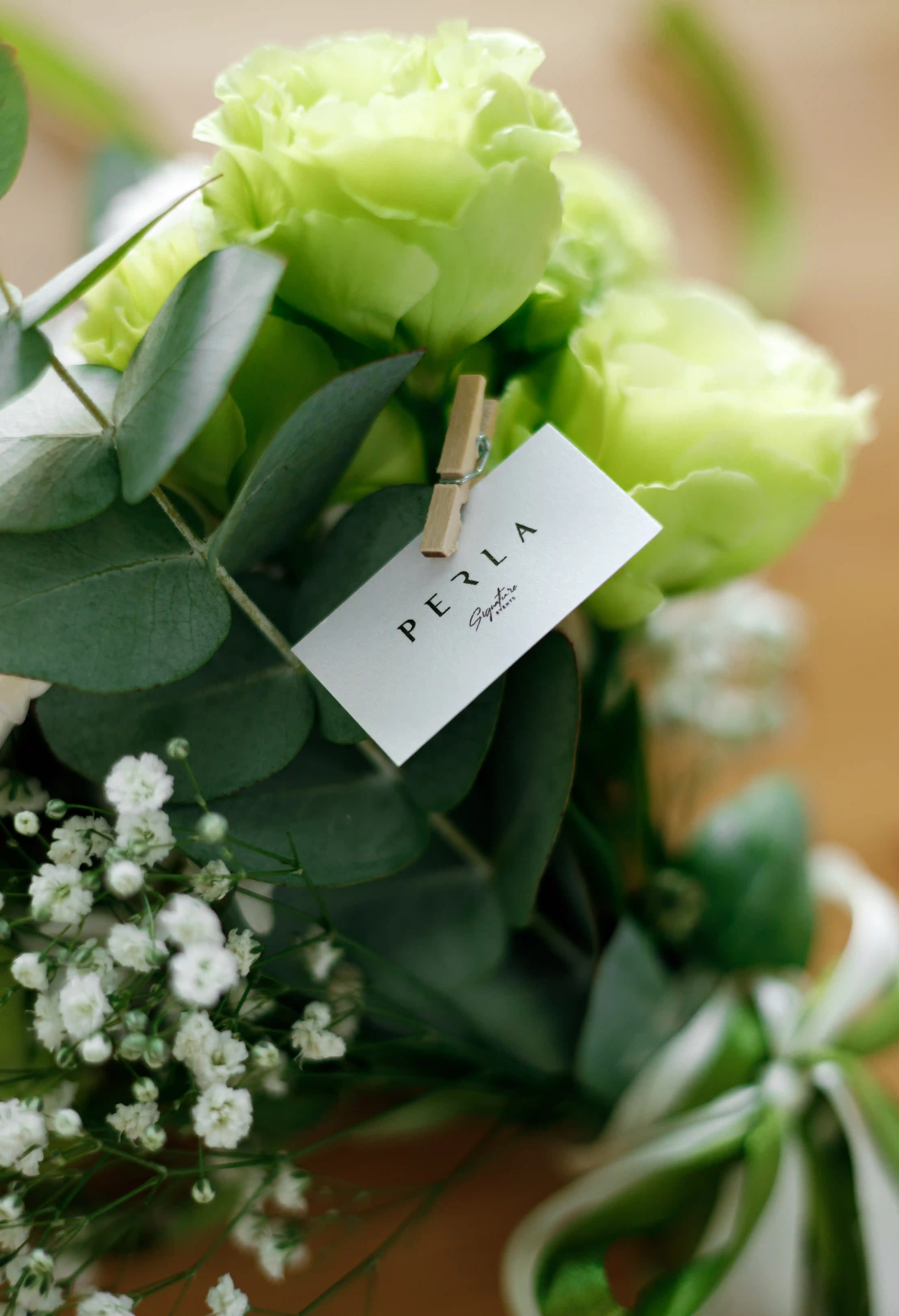 Perla Signature Events branded card clipped to a lush green lisianthus and eucalyptus bouquet with baby's breath at a luxury event in Yerevan, Armenia