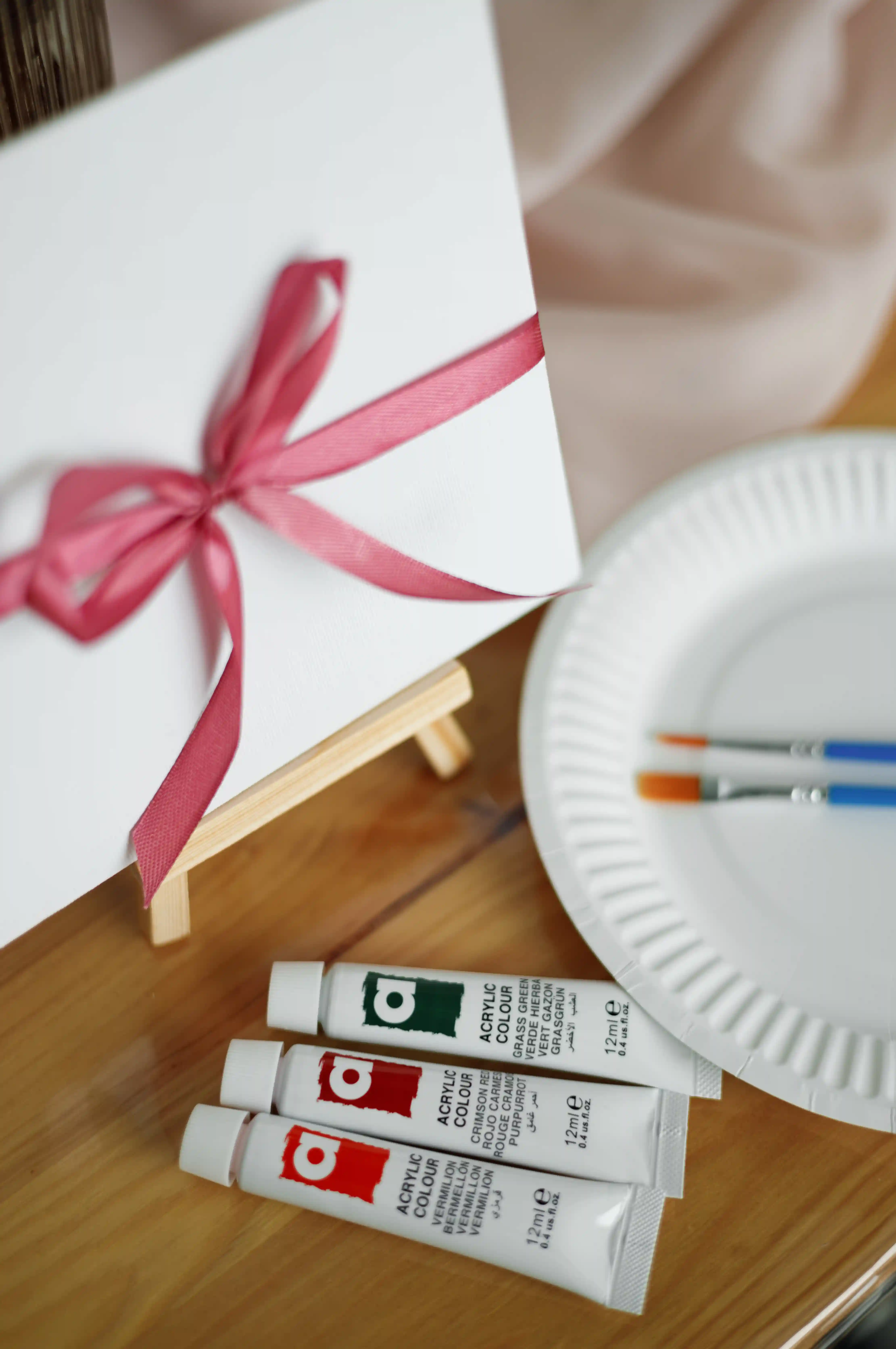 Acrylic paint tubes, brushes, and a ribbon-wrapped canvas on a mini easel set up as a guest painting activity at a luxury event by Perla Signature Events in Yerevan, Armenia