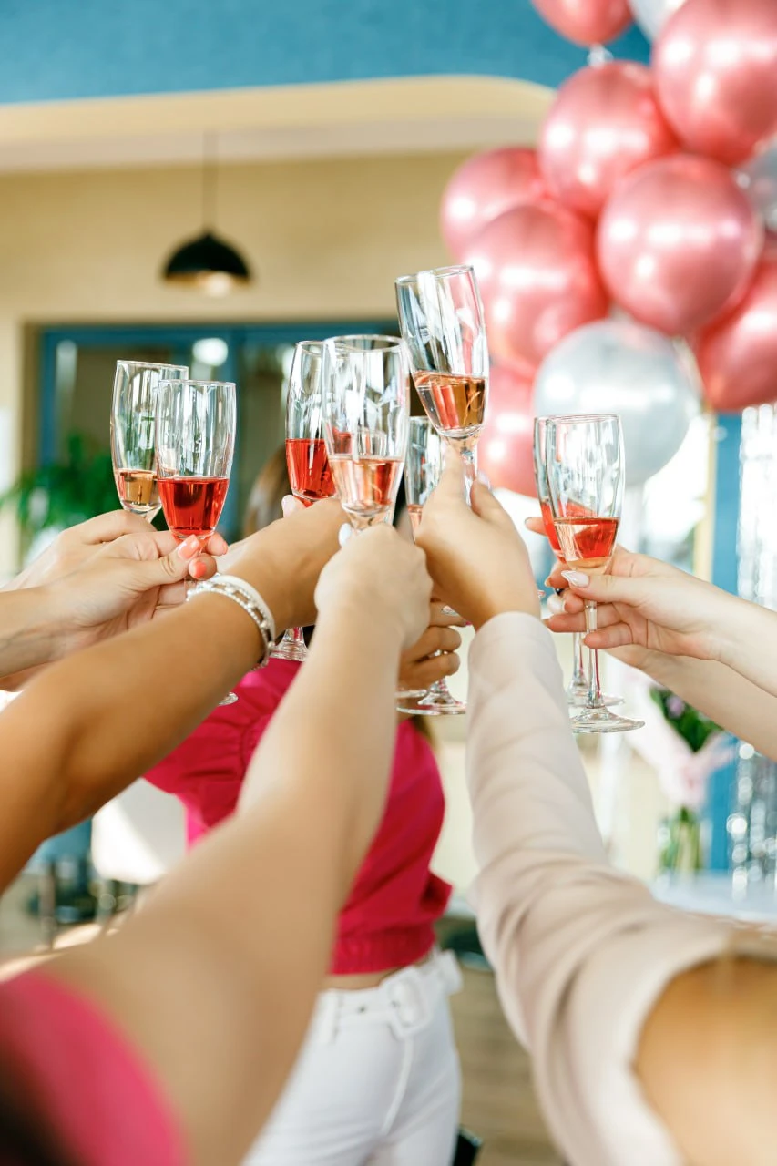 Bridal party clinking crystal champagne flutes filled with rosé in front of a rose gold and silver metallic balloon cluster at a luxury bachelorette party by Perla Signature Events in Yerevan, Armenia
