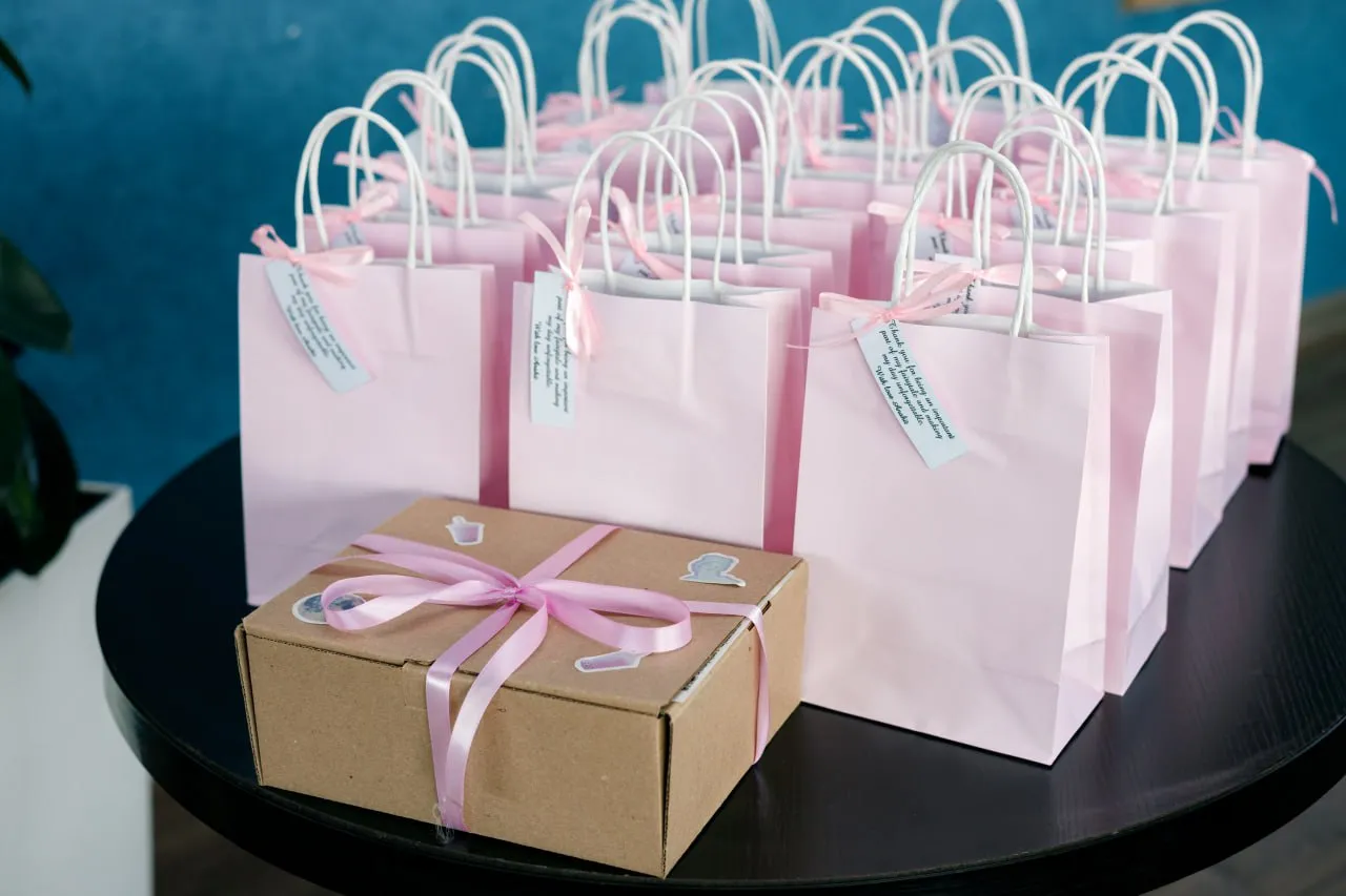 Rows of blush pink guest favor bags with personalized message tags and a kraft gift box tied with a pink satin ribbon on a black table at a luxury bachelorette party by Perla Signature Events in Yerevan, Armenia