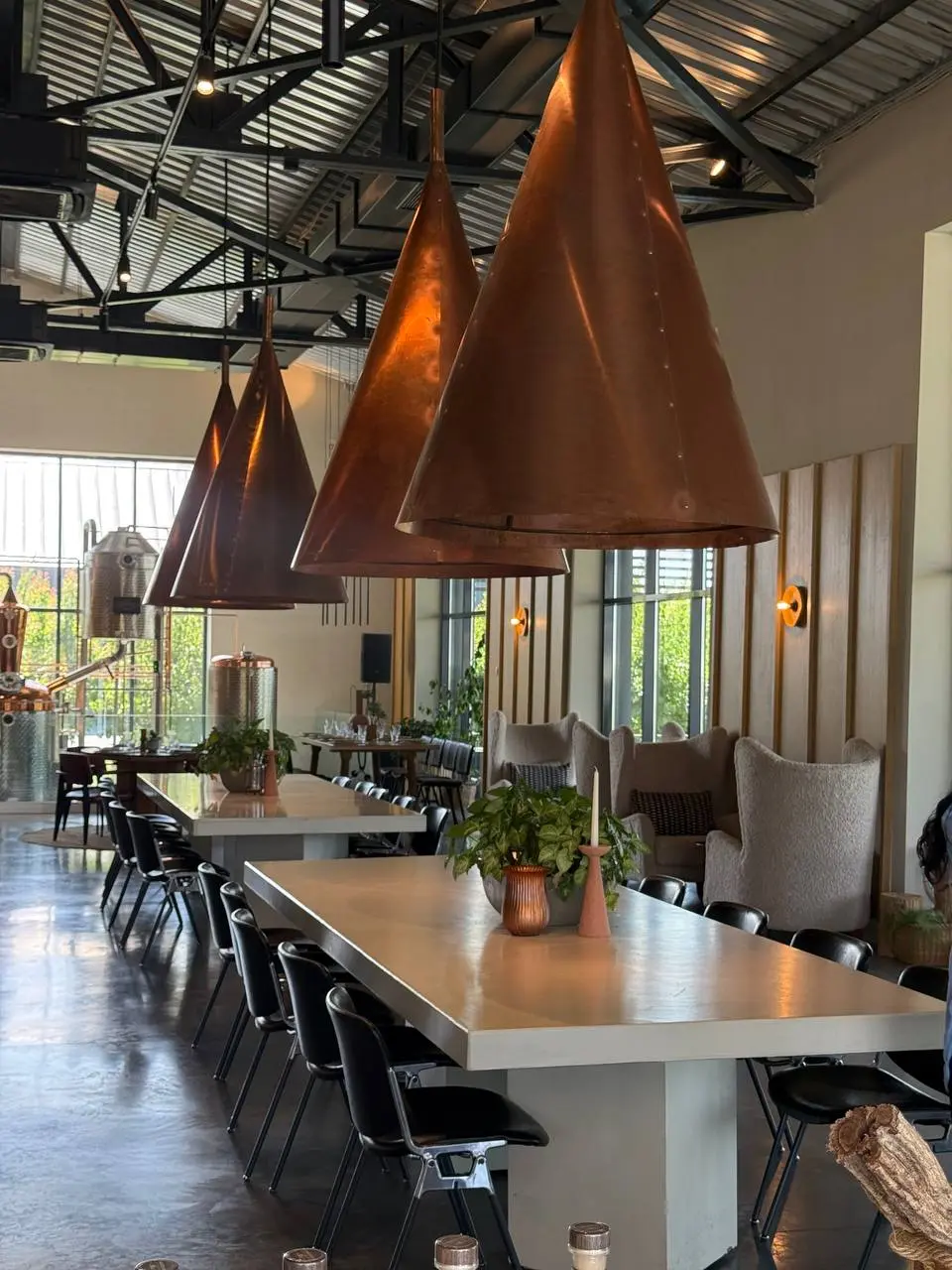 Copper cone pendant lamps above the long tables in the Art Village distillery hall