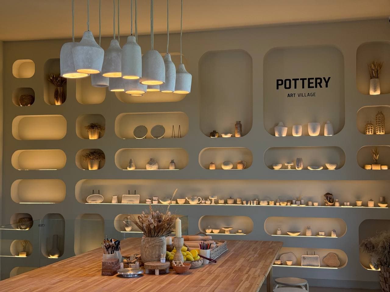 Pottery masterclass table at Art Village set with tools beneath lit display shelving