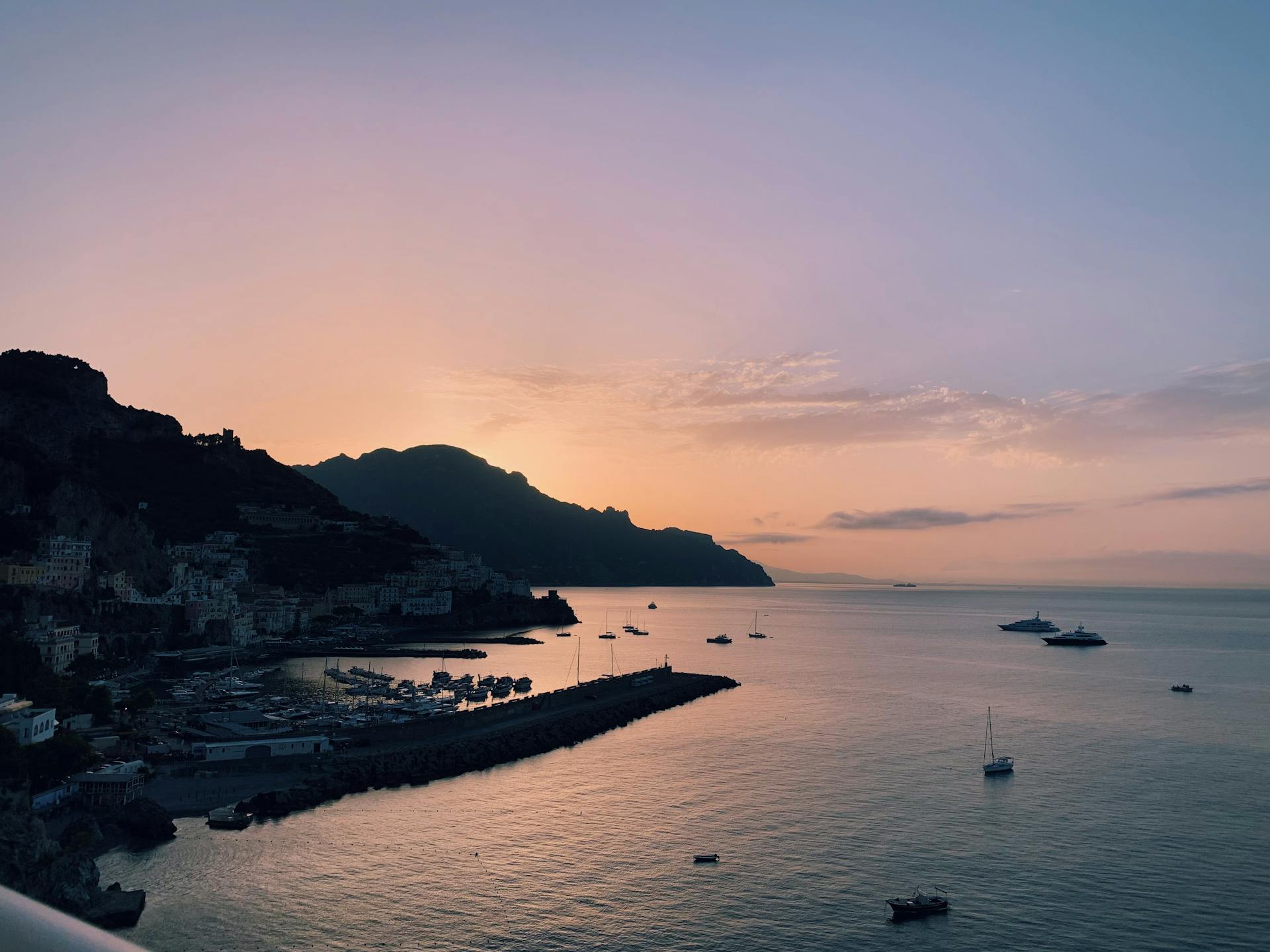 Amalfi Coast at sunset with colourful sky, cliffs, and the calm sea below.