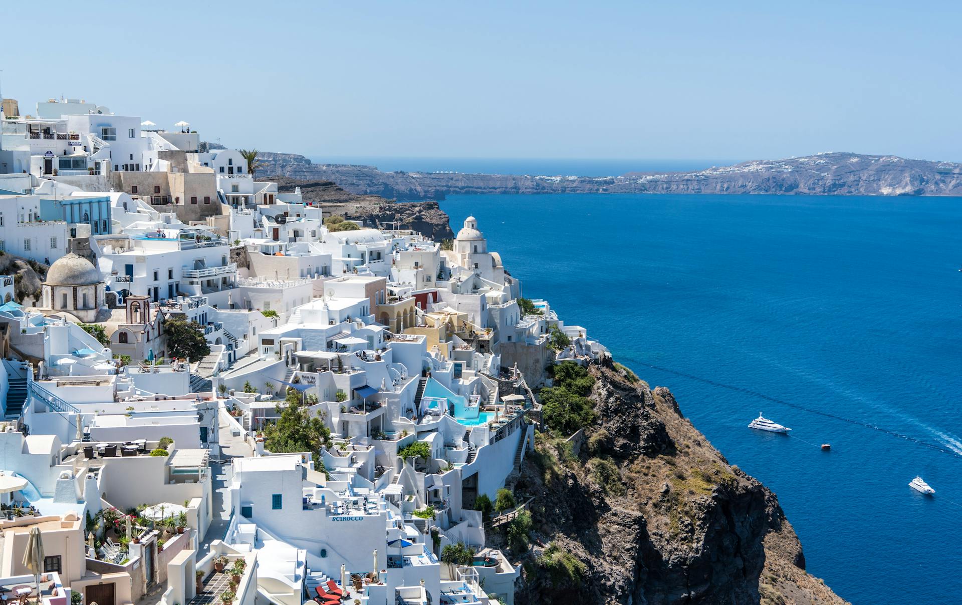 Panoramic view of Oia, Santorini, showcasing iconic white buildings with blue domes overlooking the Aegean Sea under a bright, clear sky