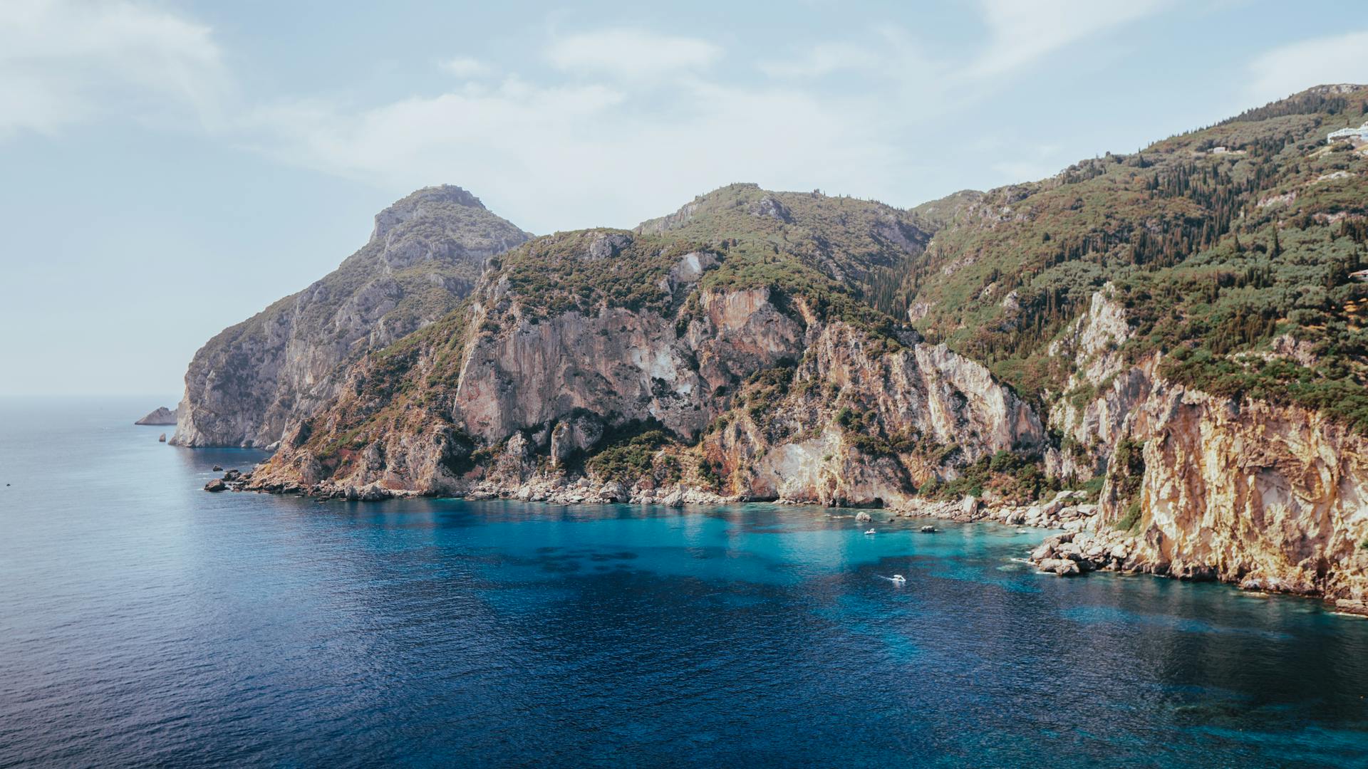 Scenic view of Corfu bay with clear blue water, rocky shoreline, and green shrubs