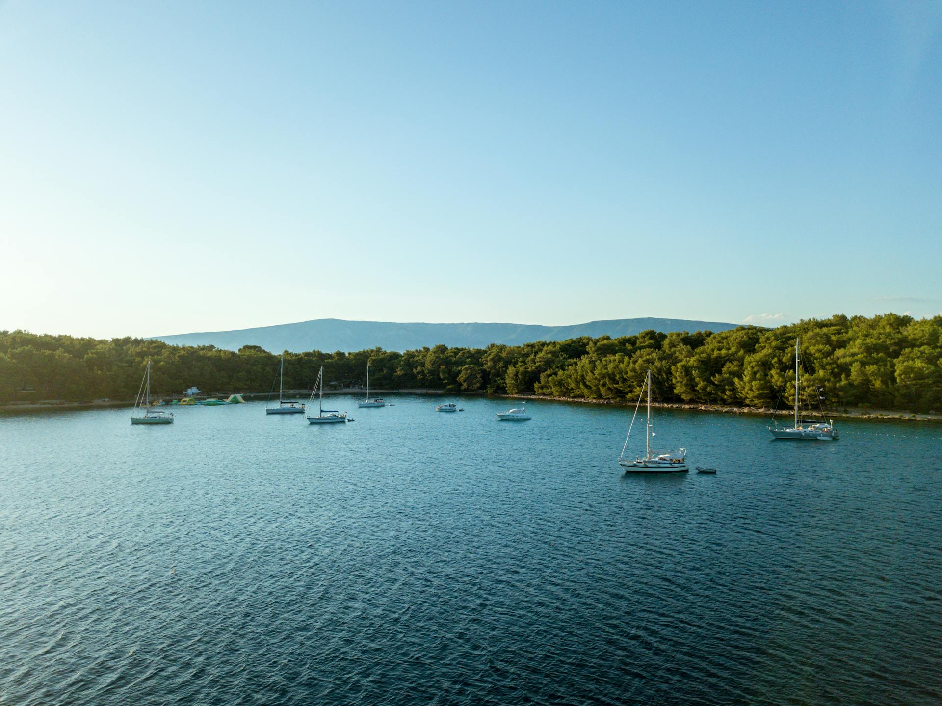 Scenic view of Hvar bay with boats anchored near the shore and a lush tree line in the background