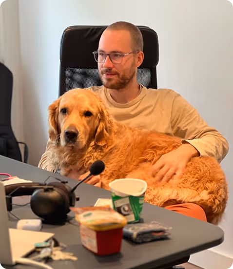 Ein Mann mit Brille sitzt auf einem Bürostuhl und hält einen goldenen Retriever auf dem Schoß.