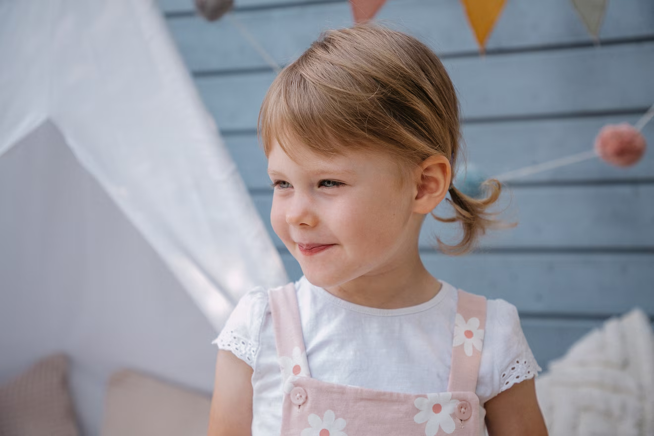 Nahaufnahme von einem jungen Mädchen, dass vor einem kleinen Zelt steht und das auf die Seite schaut.