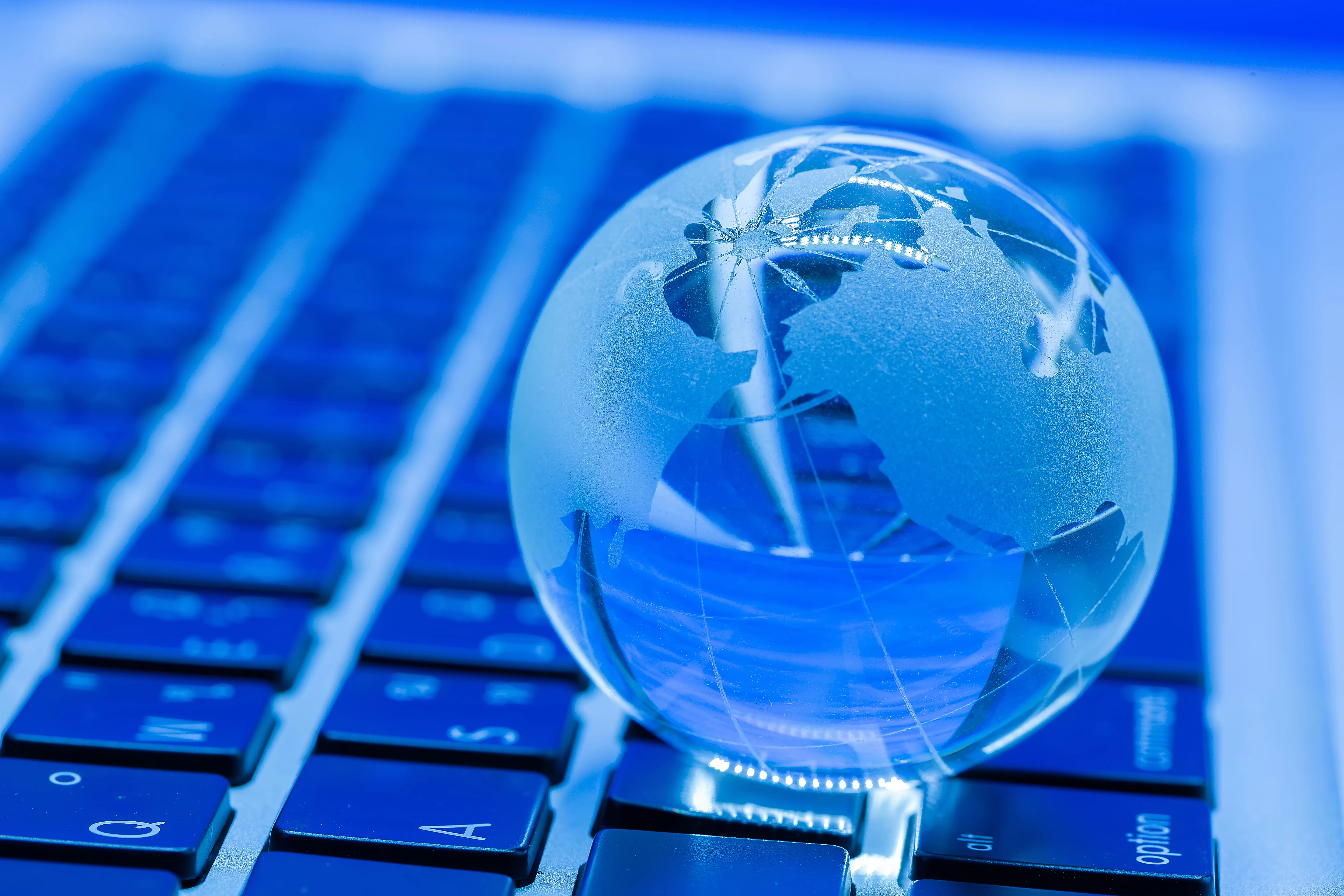 A clear globe depicting continents, resting on a laptop keyboard with a blue lighting background.