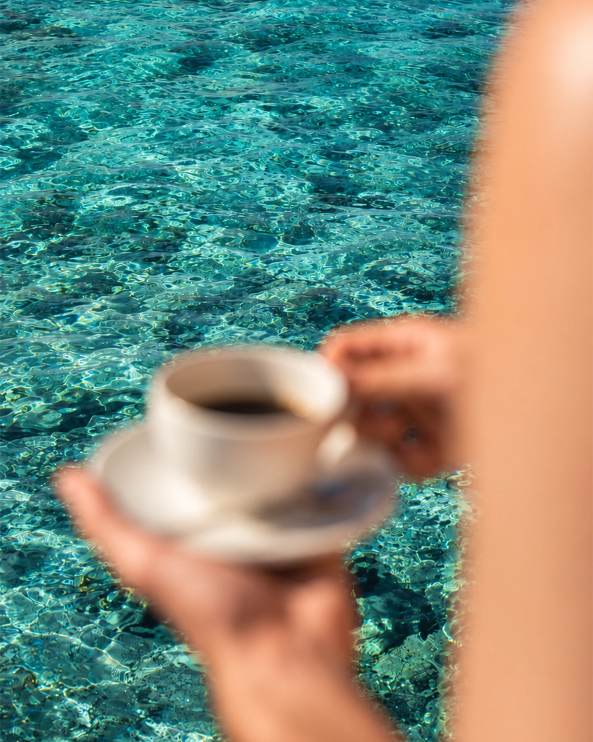 Coffee cup held beside turquoise seawater