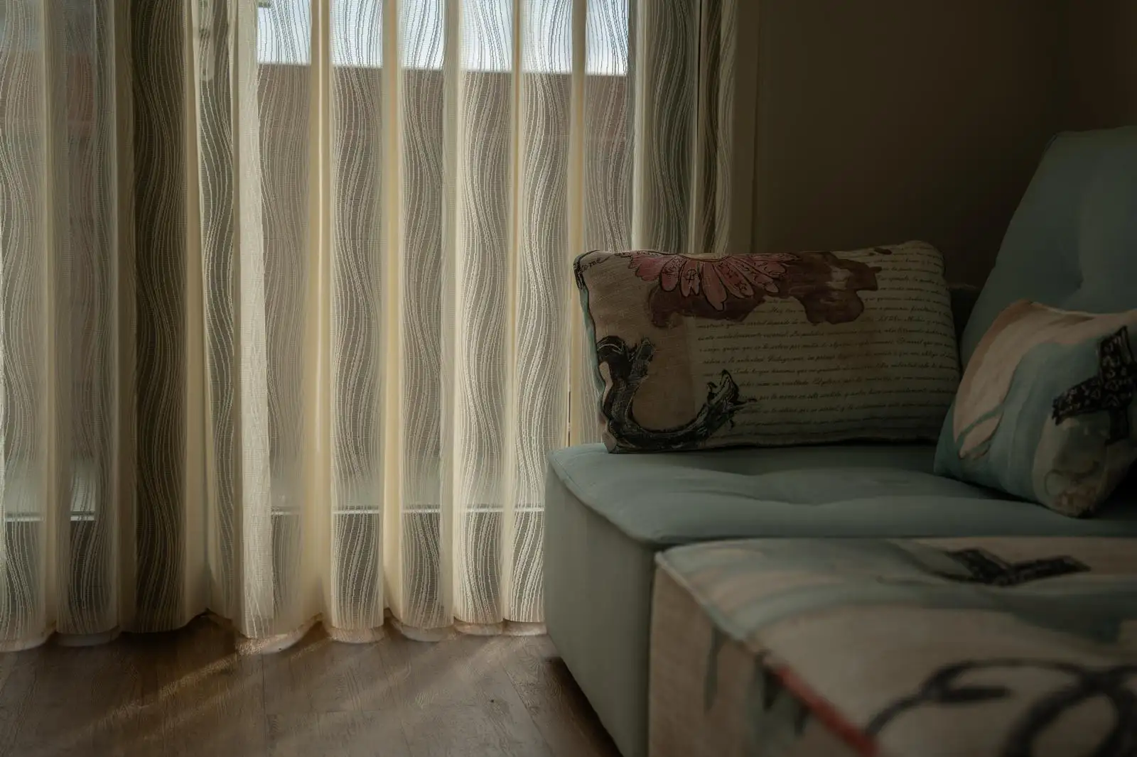 Moderne woonkamer met twee lichtgrijze banken, een houten salontafel, zwarte houten jaloezieën voor grote ramen en neutrale decoraties.