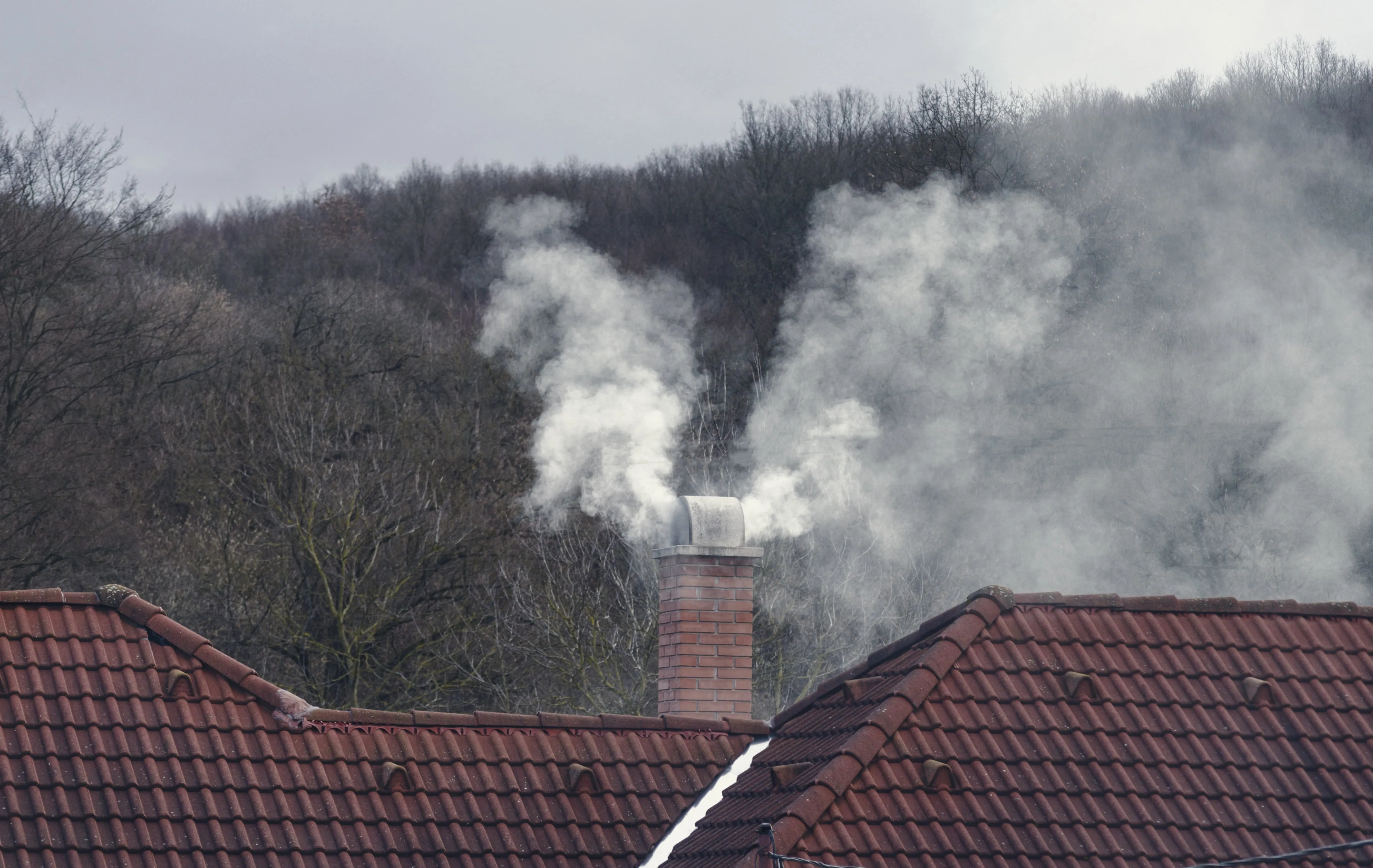 Brick chimney on a residential roof with smoke rising during winter