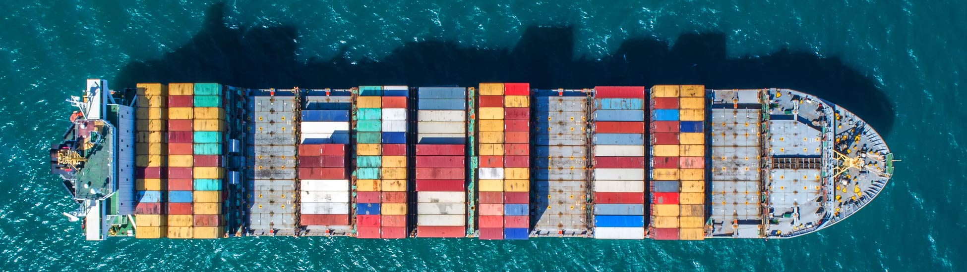 Vogelperspektive auf ein Frachtcontainerschiff mit bunten Containerstapeln auf dem blauen Meer.