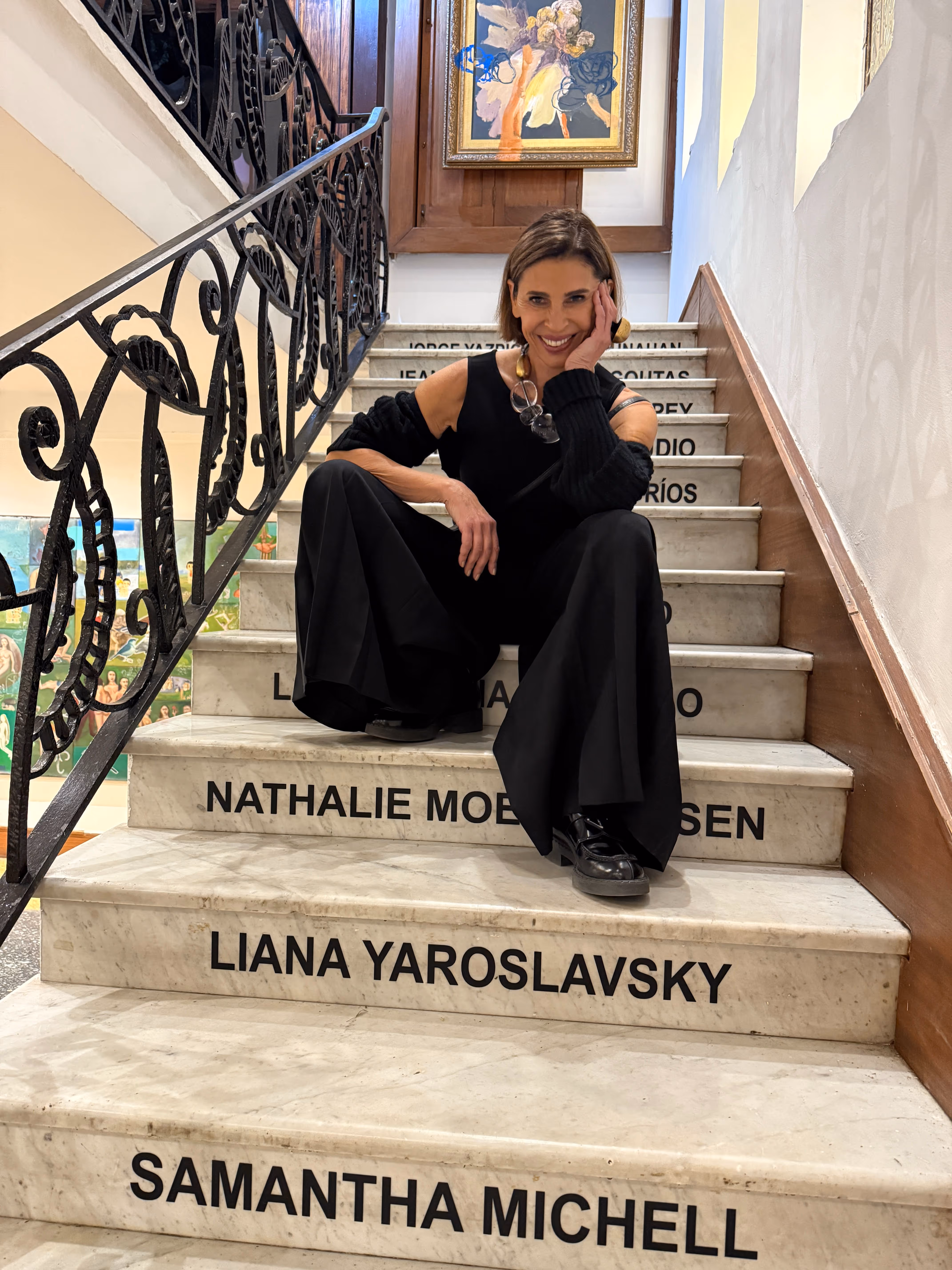 Woman in black outfit sitting on marble stairs with black iron railings and names written on the steps.