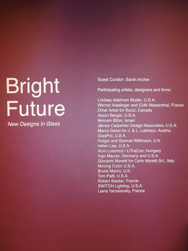 Exhibit wall titled 'Bright Future: New Designs in Glass' listing guest curator Sarah Archer and participating artists and firms from various countries.