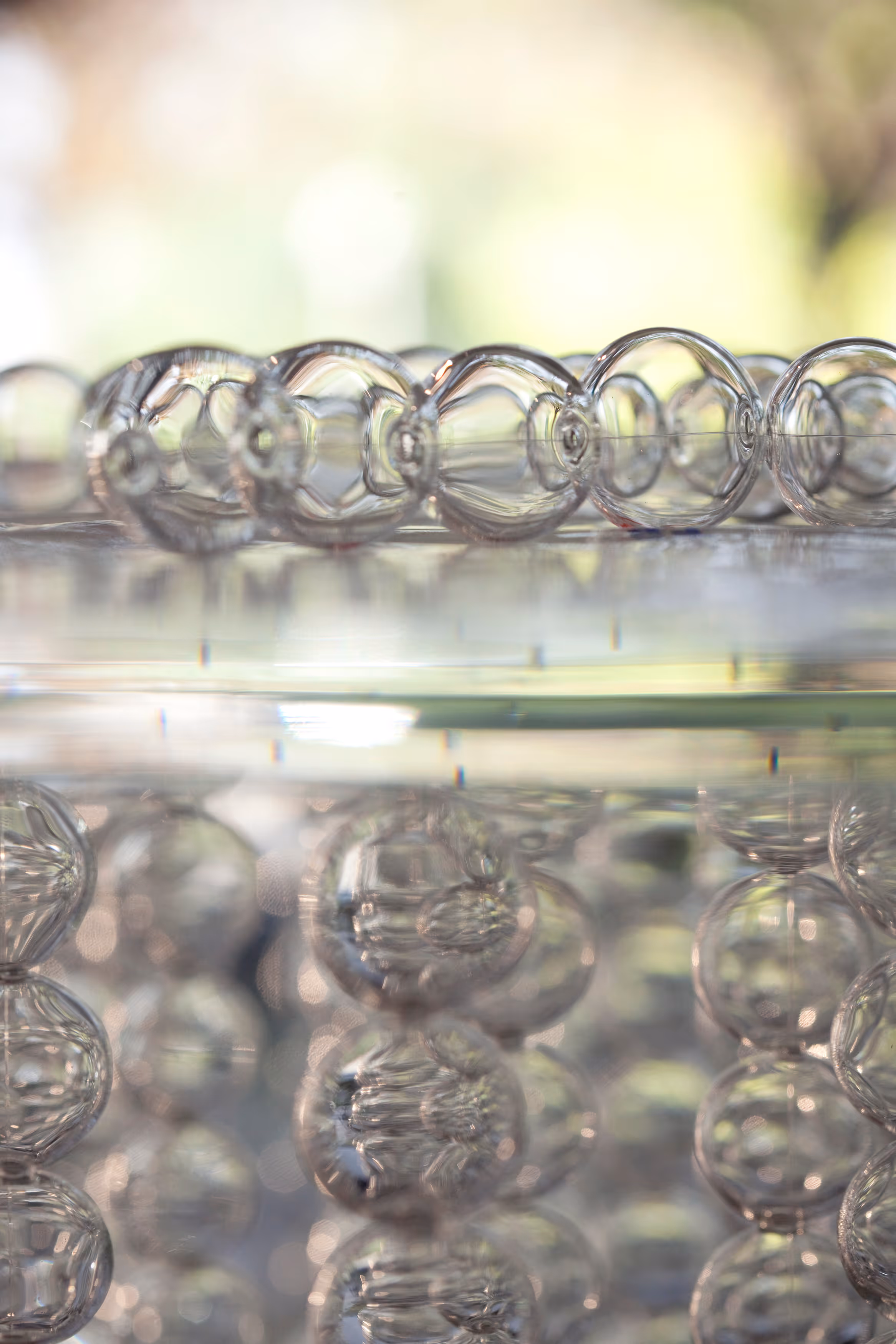 Close-up of transparent soap bubbles floating on water with blurred green and yellow background.