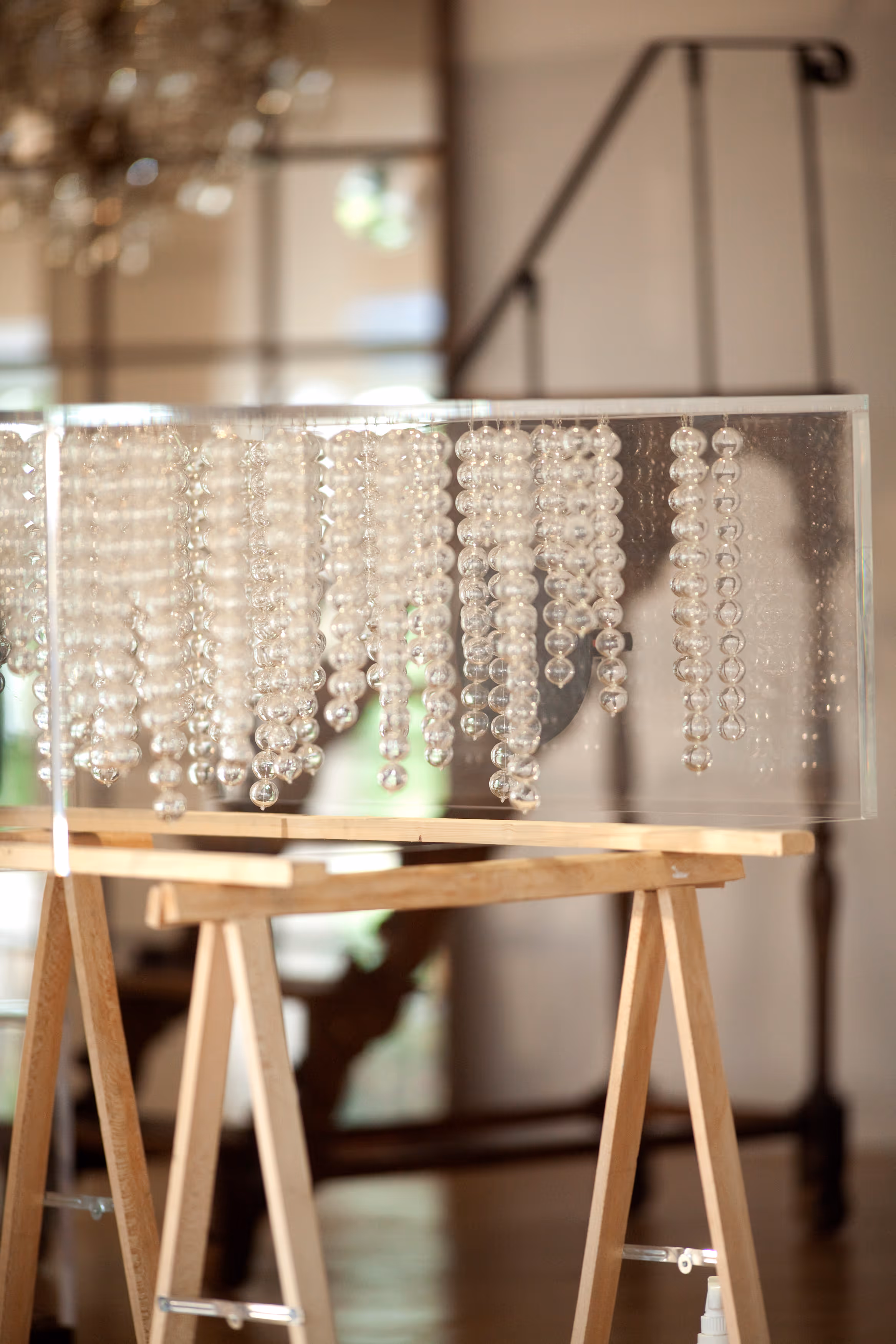 Decorative art piece with clear glass beads hanging inside a transparent rectangular box supported by a wooden frame.