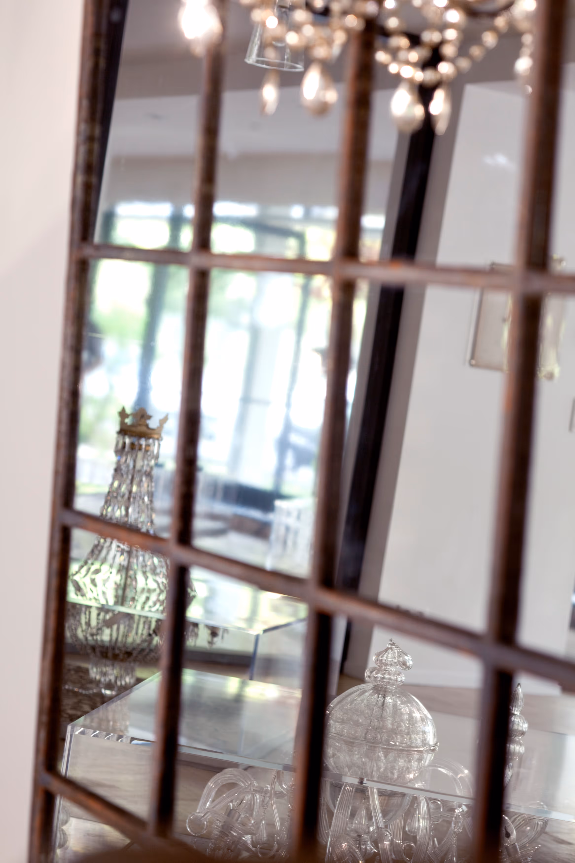 Reflection of a crystal chandelier with a crown ornament and decorative glass pieces seen through a multi-pane window.