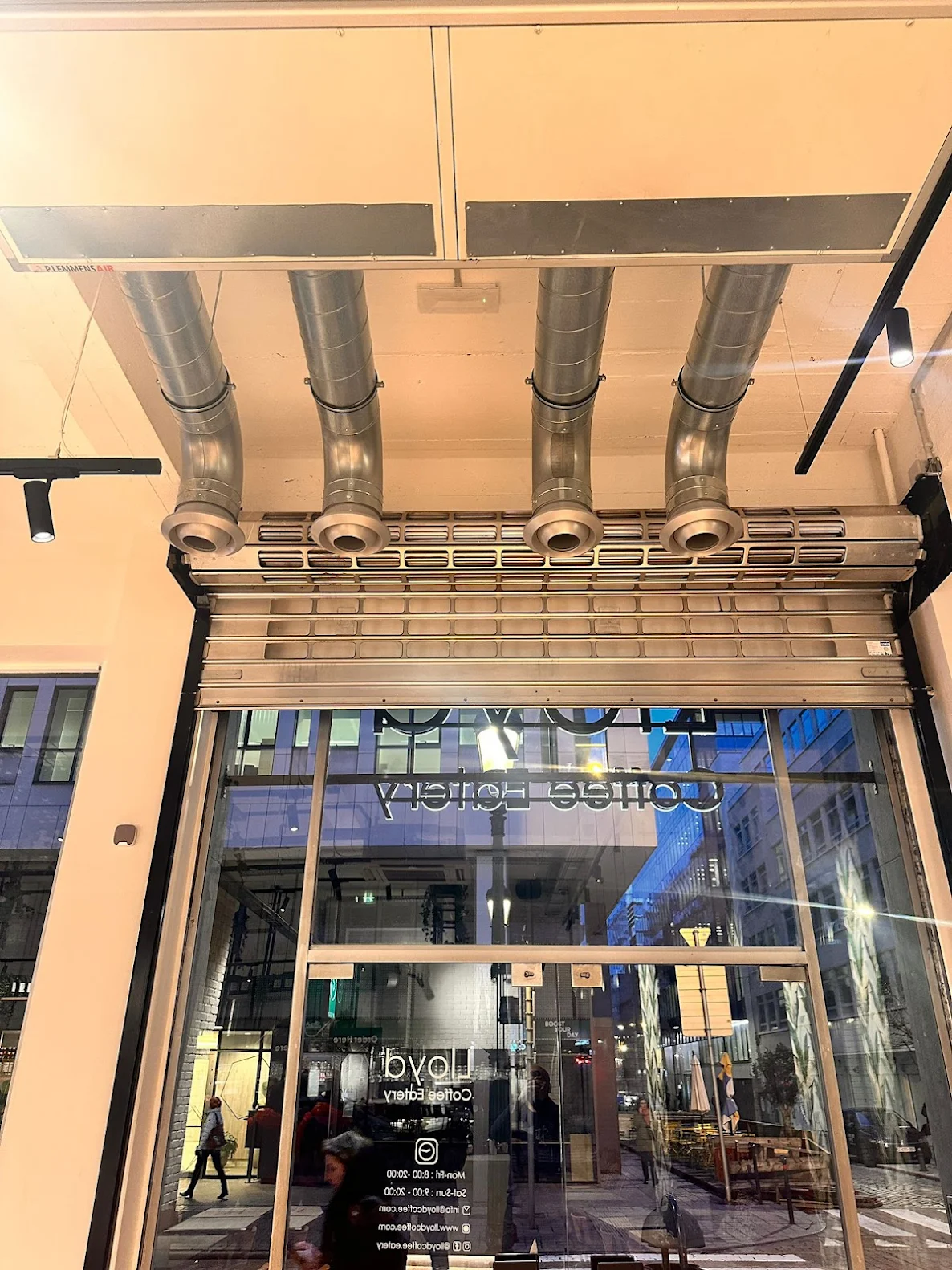 Interior view of a coffee shop entrance with large glass door and silver ventilation ducts on the ceiling.
