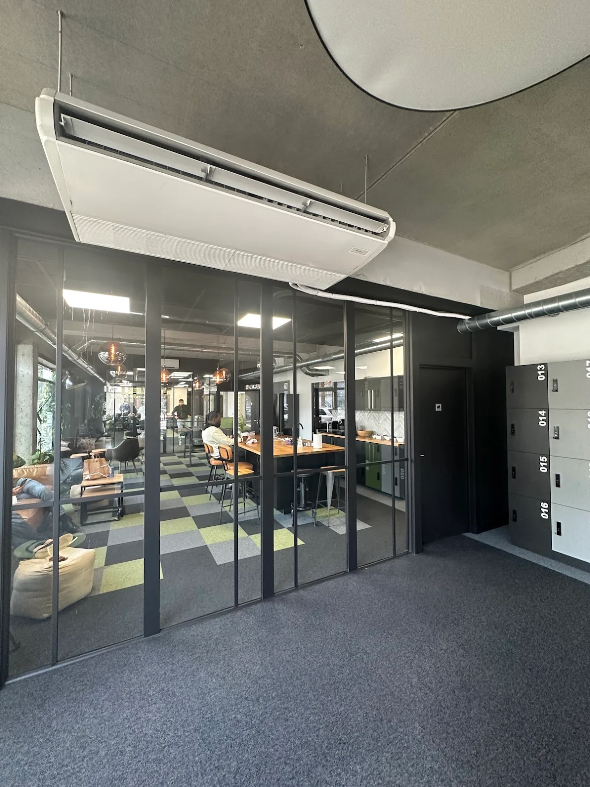 Modern office space with glass walls, colorful checkered carpet, a wooden meeting table, and a person working inside.