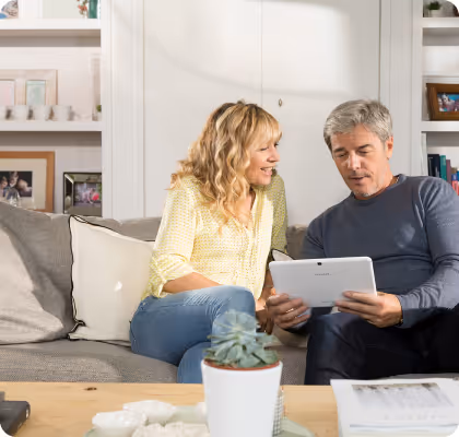 Middle-aged couple sitting on a couch looking at a tablet together in a cozy living room.