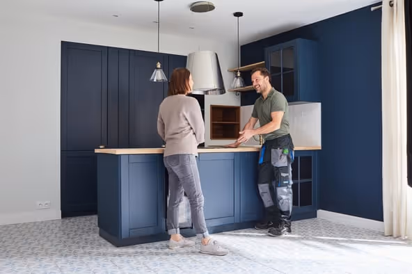 Worker installing or demonstrating a kitchen oven to a woman in a modern kitchen with dark blue cabinets and patterned floor tiles.
