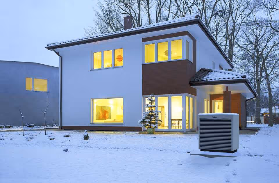 Modern two-story house with warm interior lights and snow-covered yard during dusk.