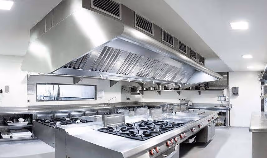Cuisine professionnelle blanche avec grandes plaques de cuisson en acier inoxydable et hotte aspirante industrielle.