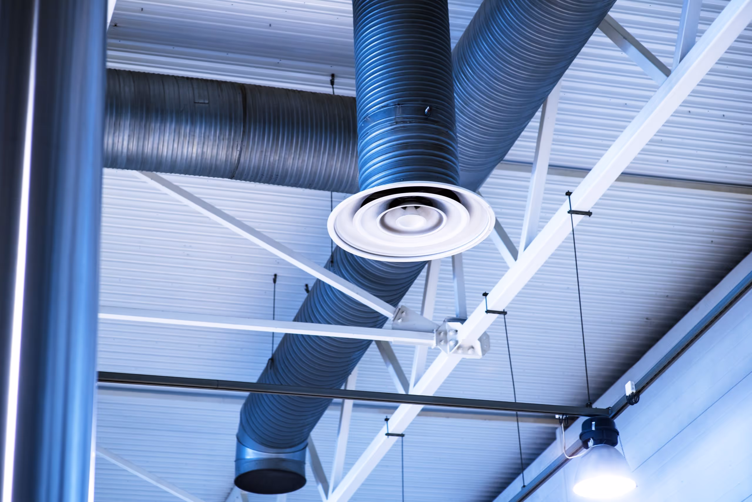 Conduits de ventilation bleus suspendus au plafond d'un bâtiment industriel avec une lampe suspendue allumée.