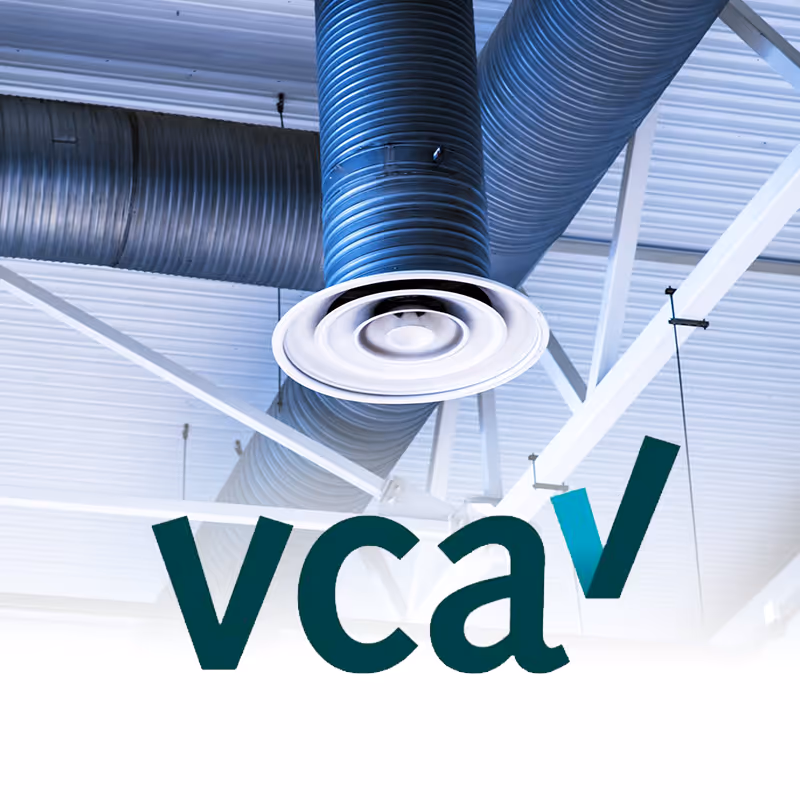 Conduits de ventilation bleus suspendus au plafond d'un bâtiment industriel avec le logo VCA en premier plan.